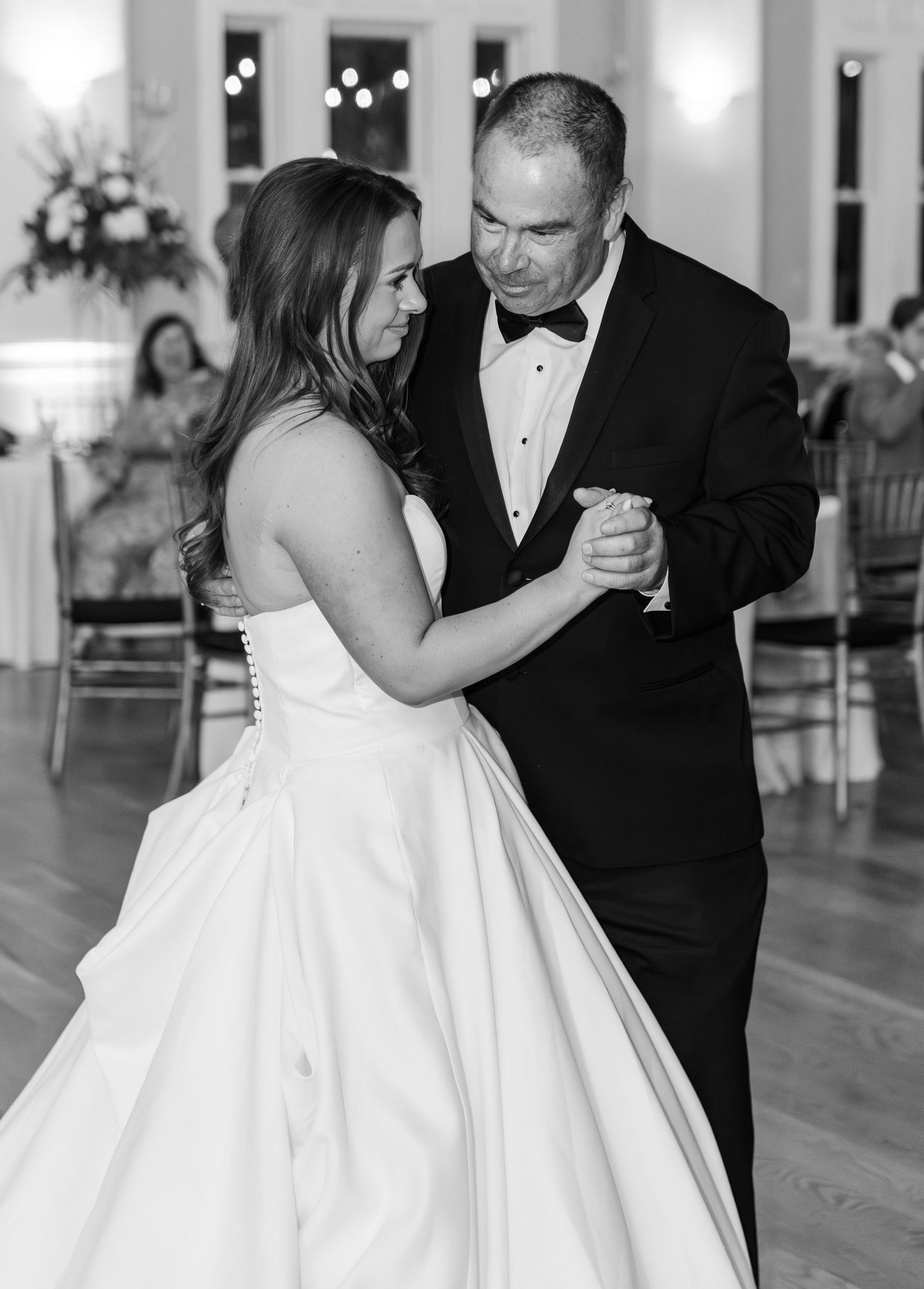 Bride and father share an emotional first dance at wedding reception in black and white photo.
