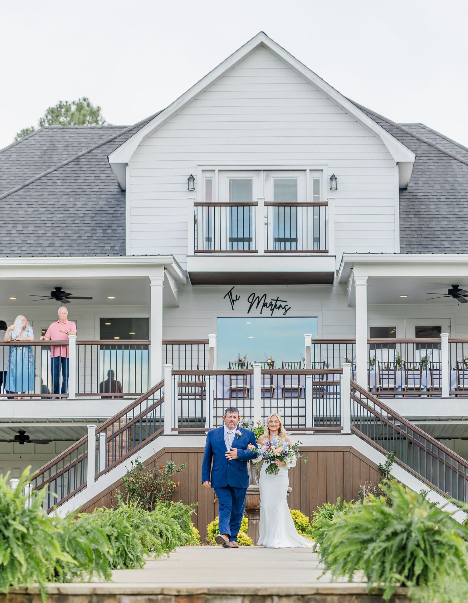 A bride and groom walk hand-in-hand outside a elegant white wedding venue building.