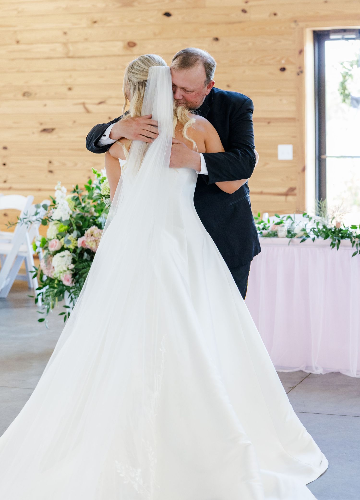 Bride and father share emotional first dance in rustic barn wedding venue with floral decor.