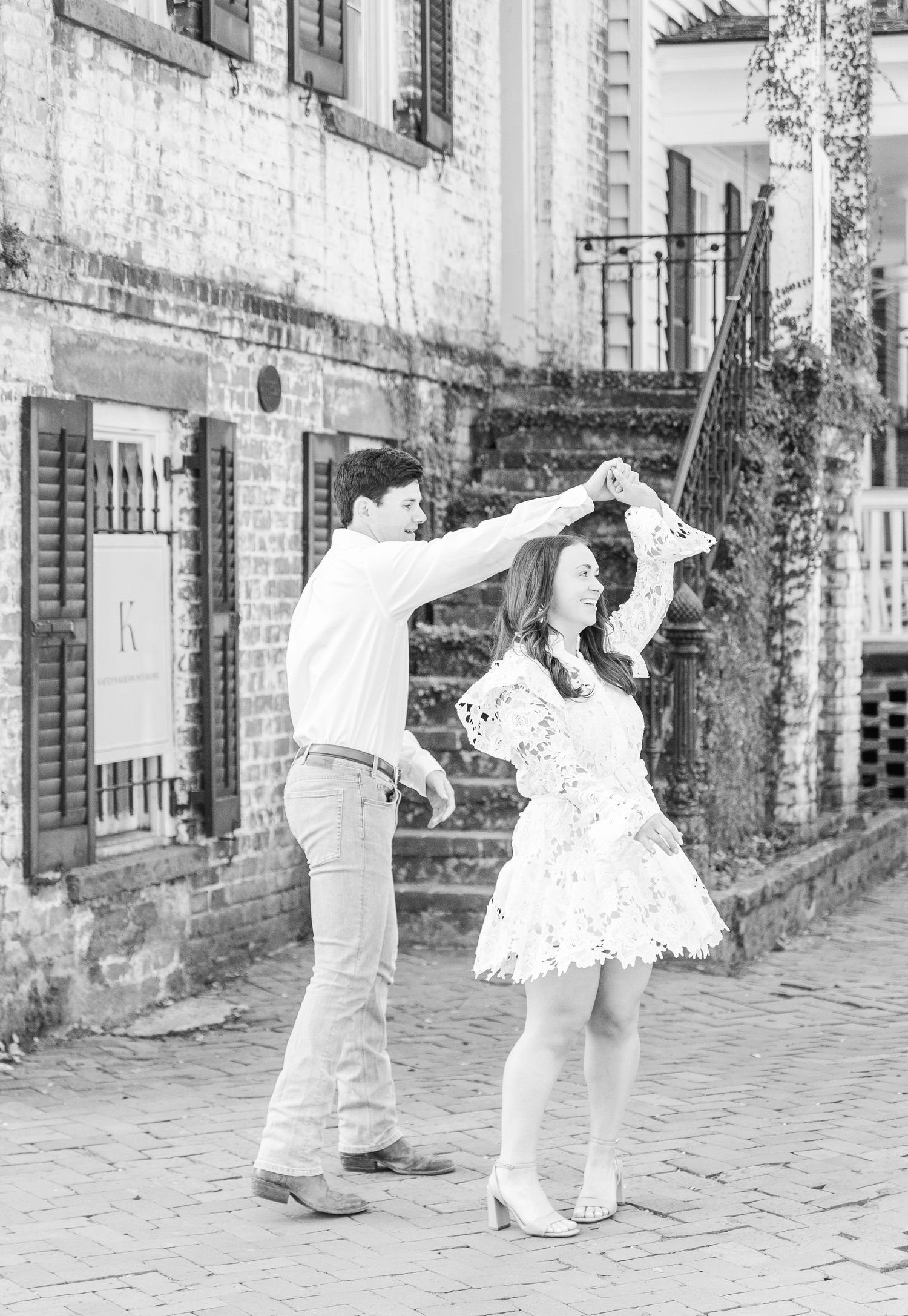 Black and white image of a couple dancing on brick pavement near historic architecture.