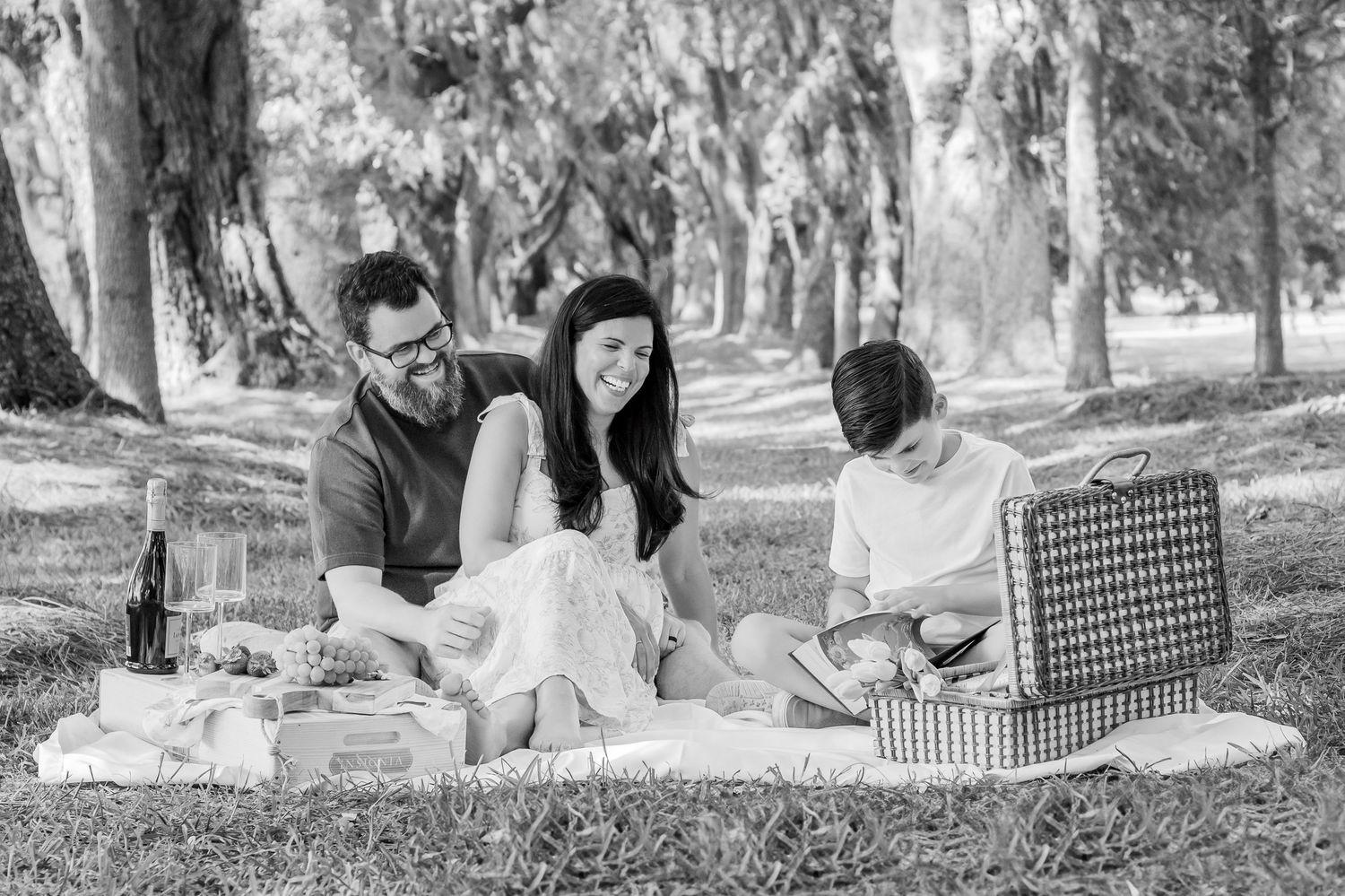 A family enjoys a picnic on a blanket under moss-covered trees in a peaceful park setting.