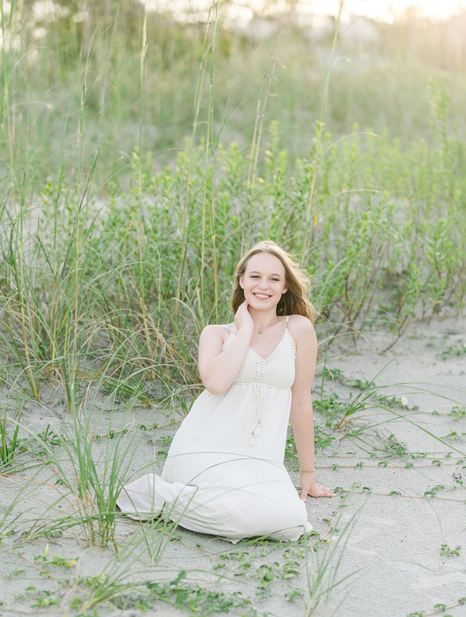 Ethereal beach portrait with long white dress against coastal dunes and sea grass.
