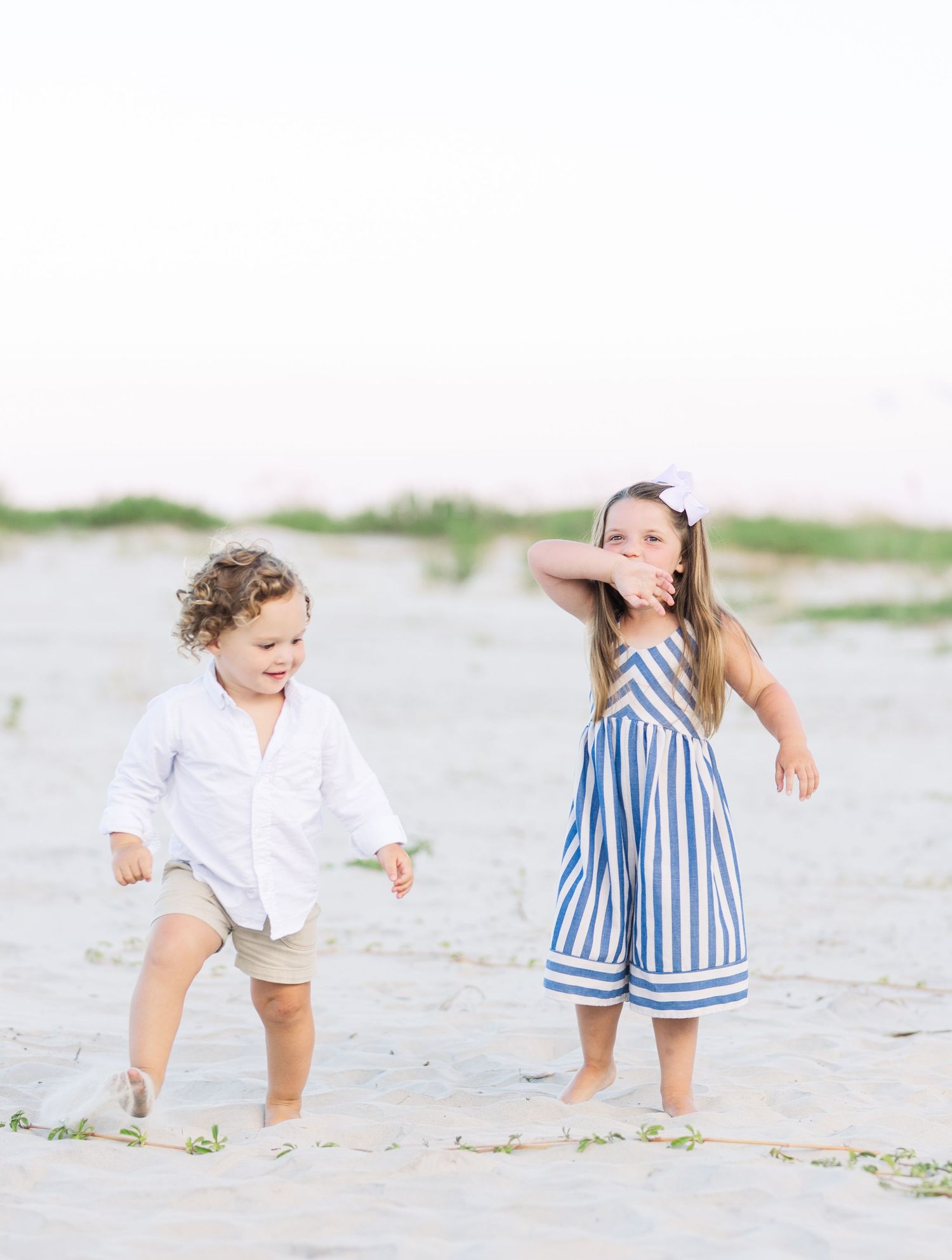 Two children dance and play together on a sandy beach.