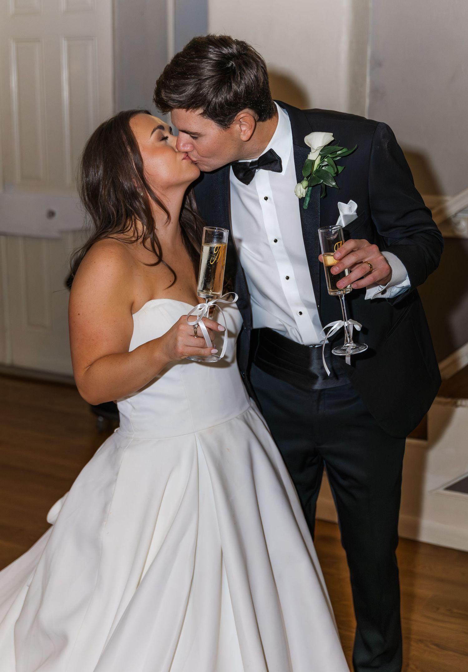 Newlyweds share a kiss while holding champagne flutes during their wedding reception celebration.