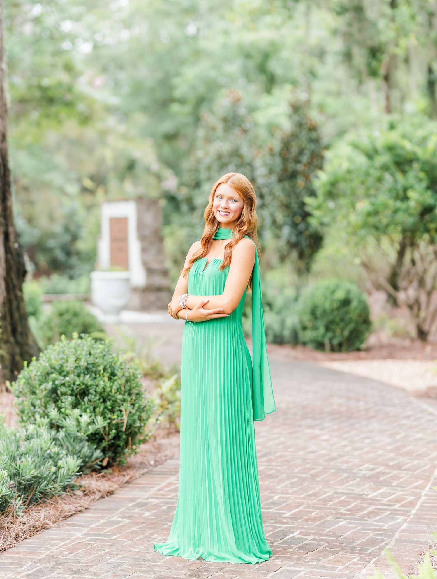 elegant shots in a flowing emerald green gown on a brick pathway surrounded by lush greenery.