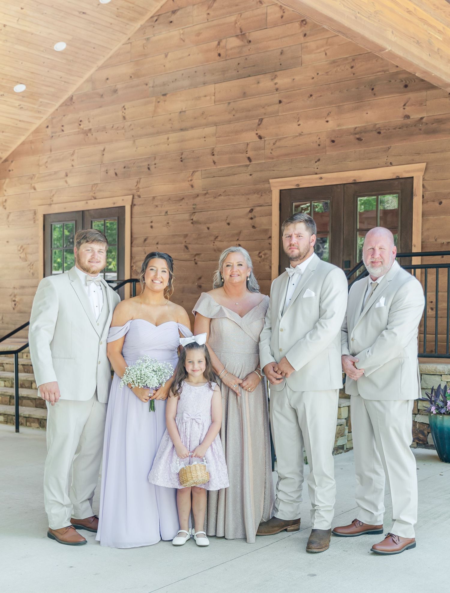 Wedding party members in light colored attire pose together on a rustic wooden porch.