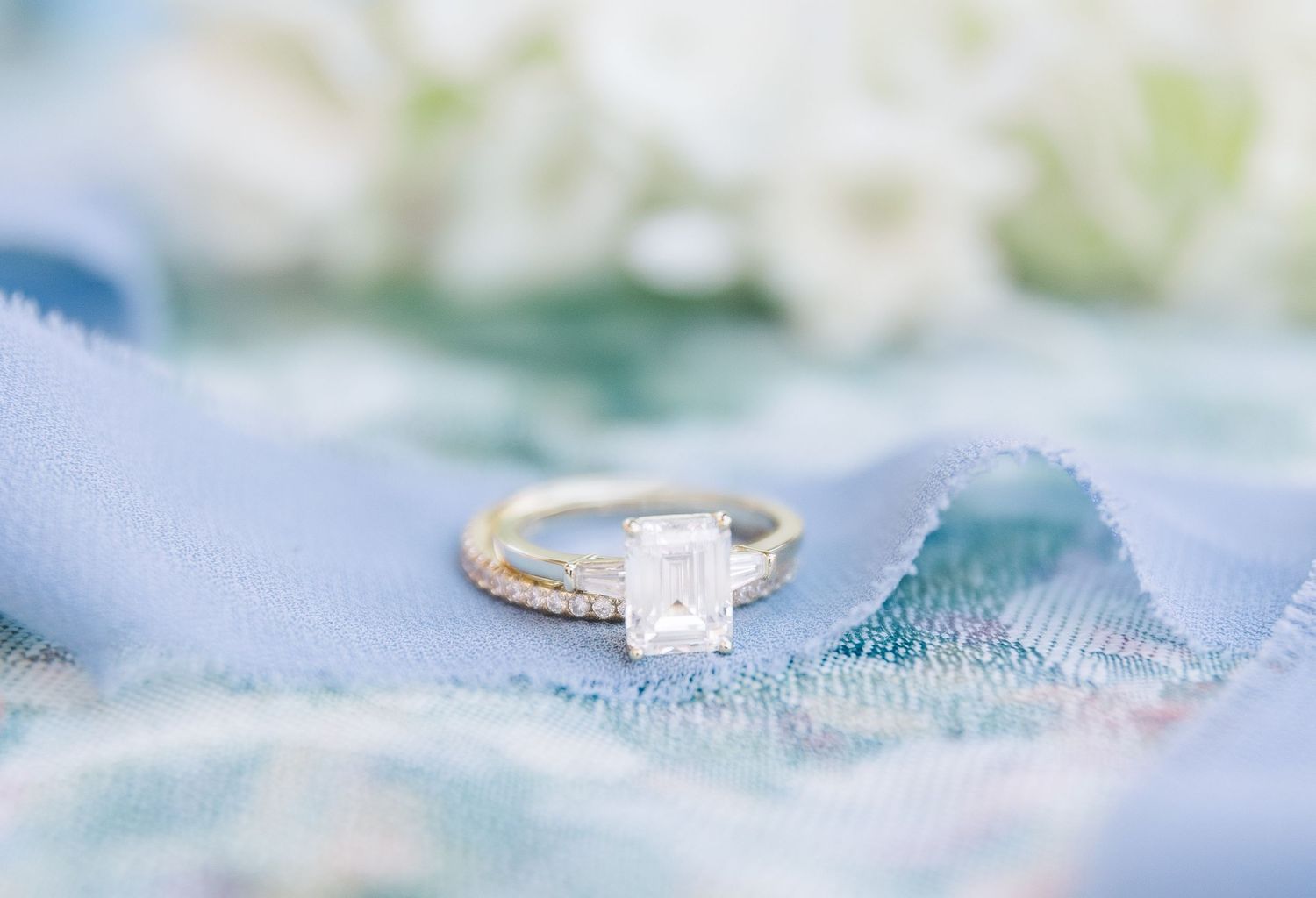 Elegant solitaire engagement ring with a square cut diamond rests on a soft blue and white textile background.