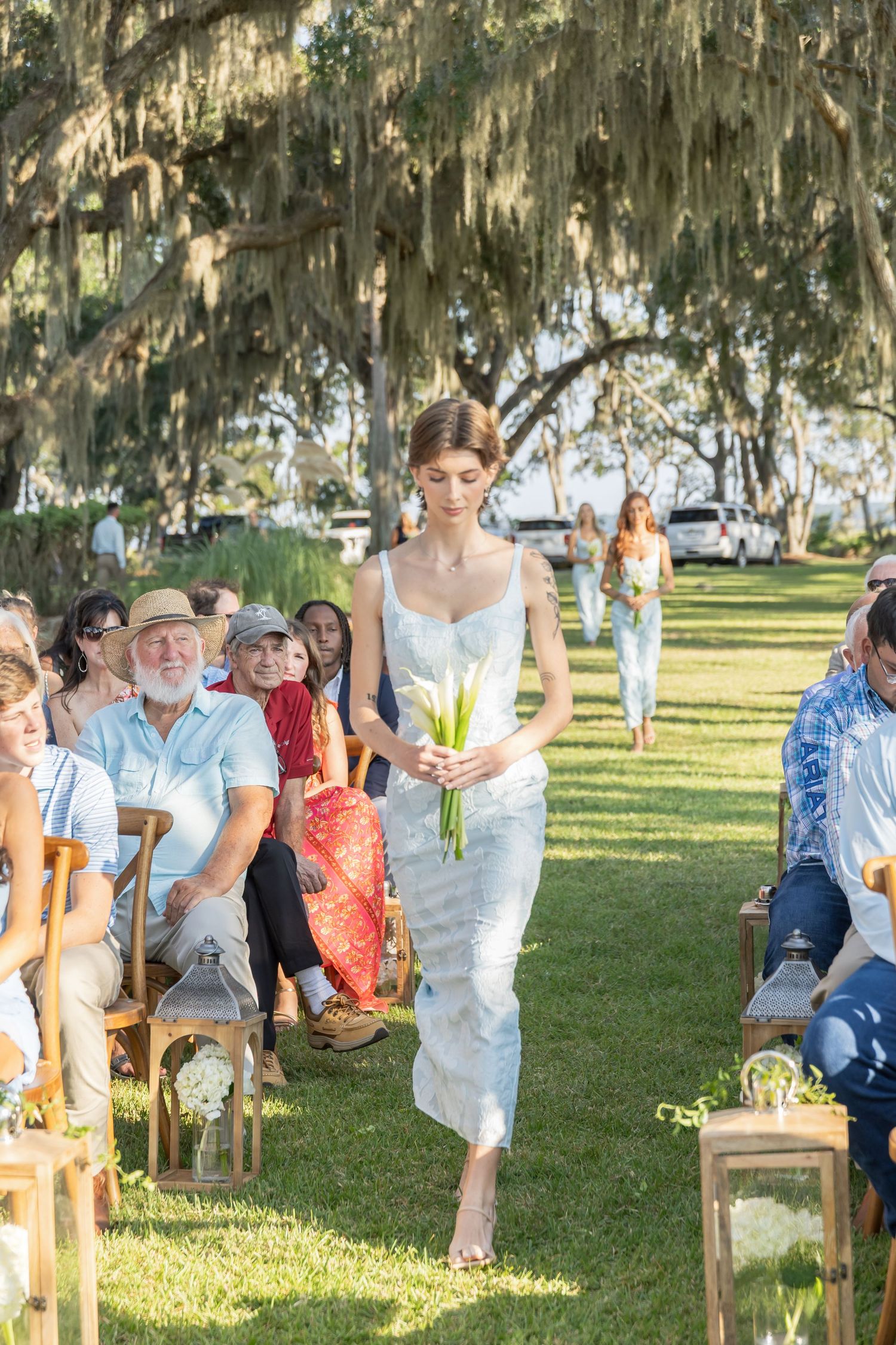 Outdoor wedding ceremony setup with wooden chairs and Spanish moss trees creating a natural canopy.