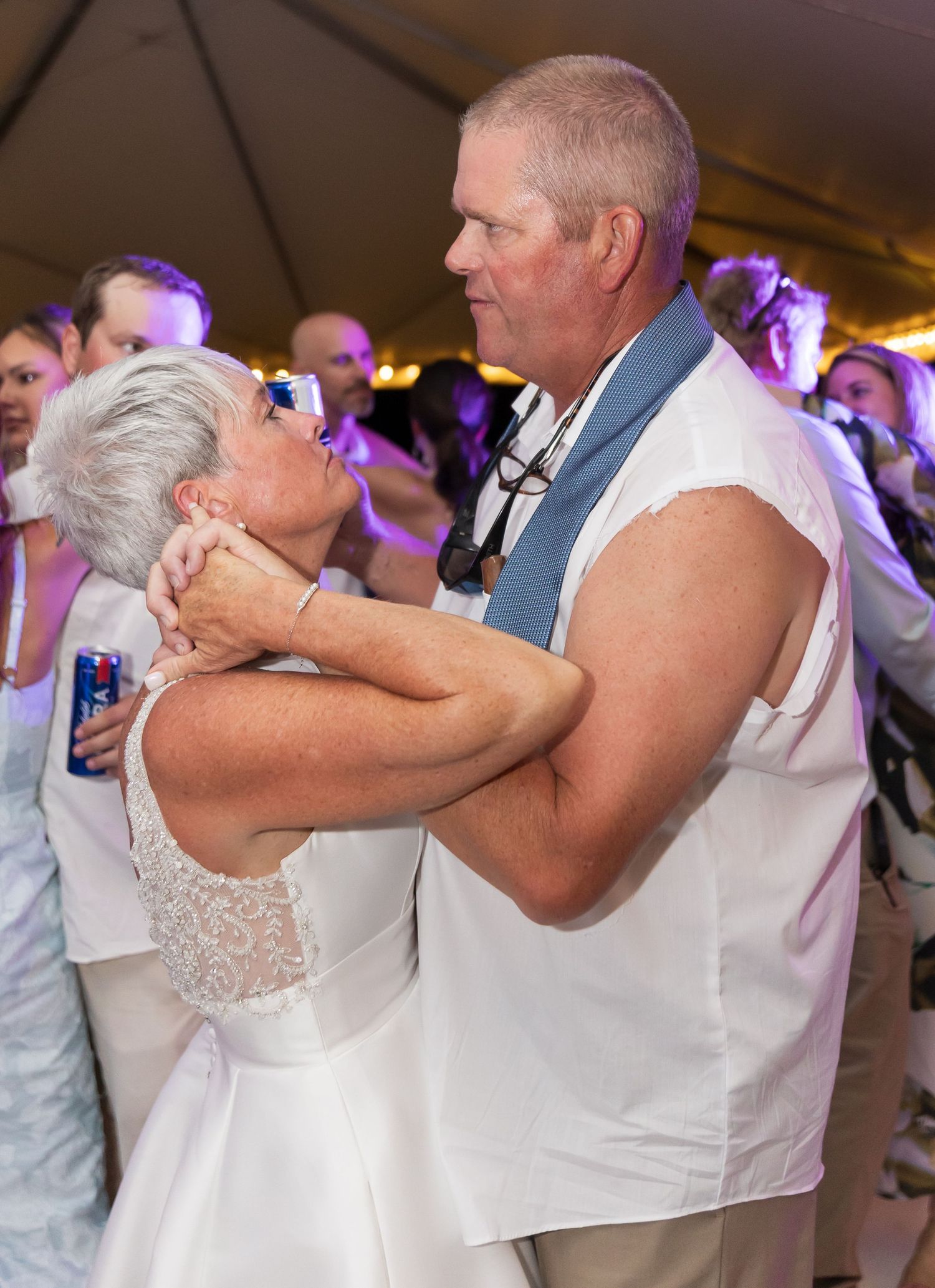 Couples slow dance together during an intimate moment at a wedding reception under warm lighting.