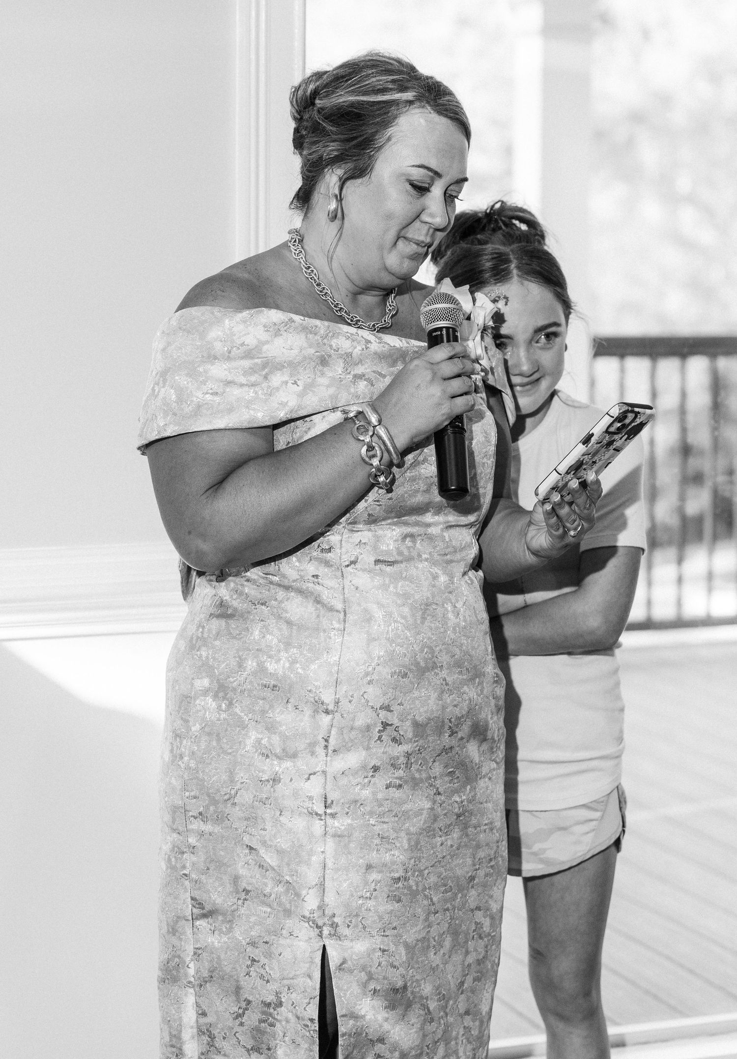 Black and white photo of woman giving wedding speech while young girl assists with notes.