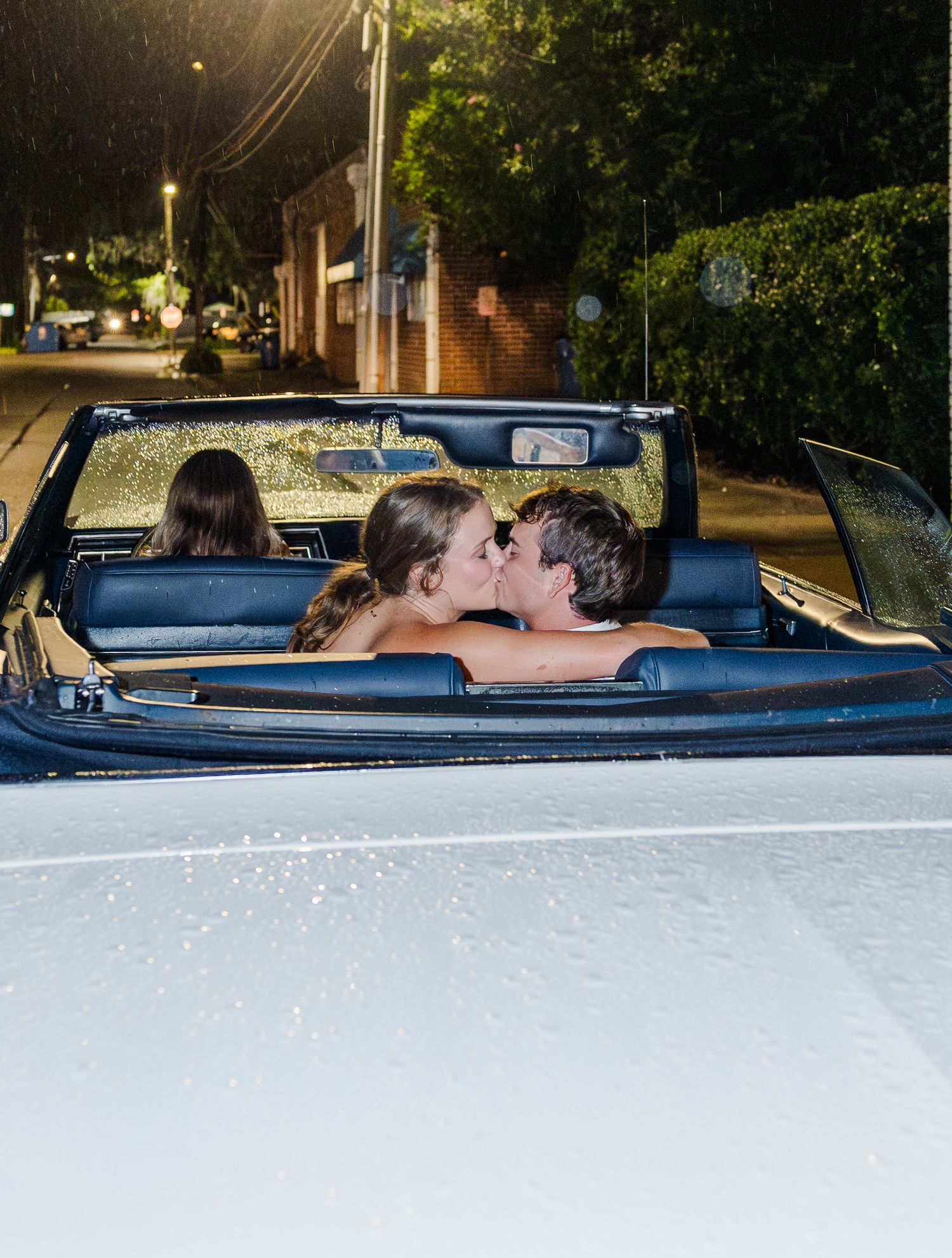 Newlyweds share romantic kiss in classic convertible car after evening wedding celebration.