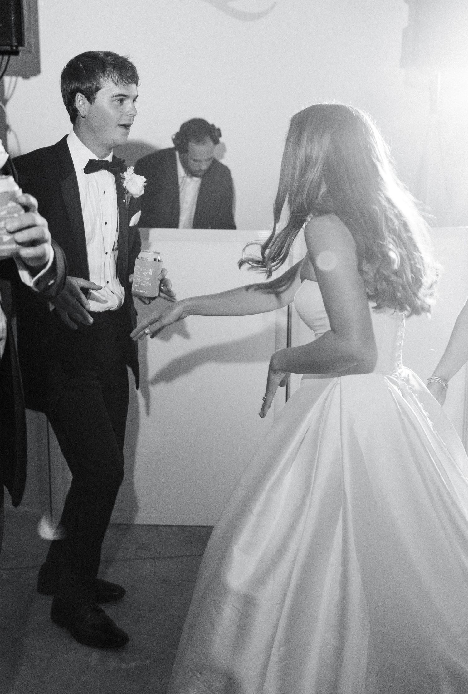 Black and white photo of bride and groom dancing joyfully at their wedding reception near the DJ booth.