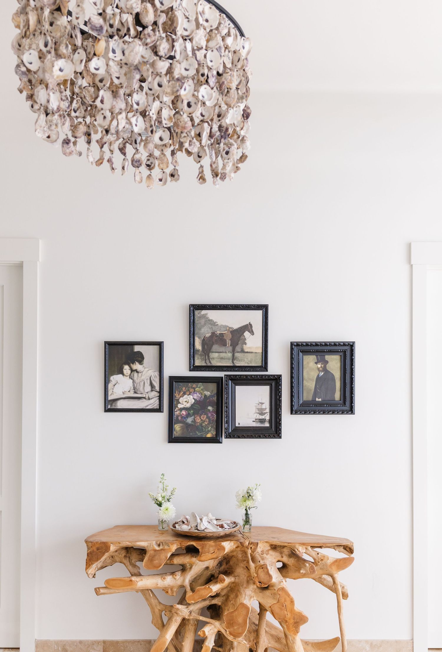 Rustic twig console table beneath a shell chandelier with a gallery wall of vintage framed photos.