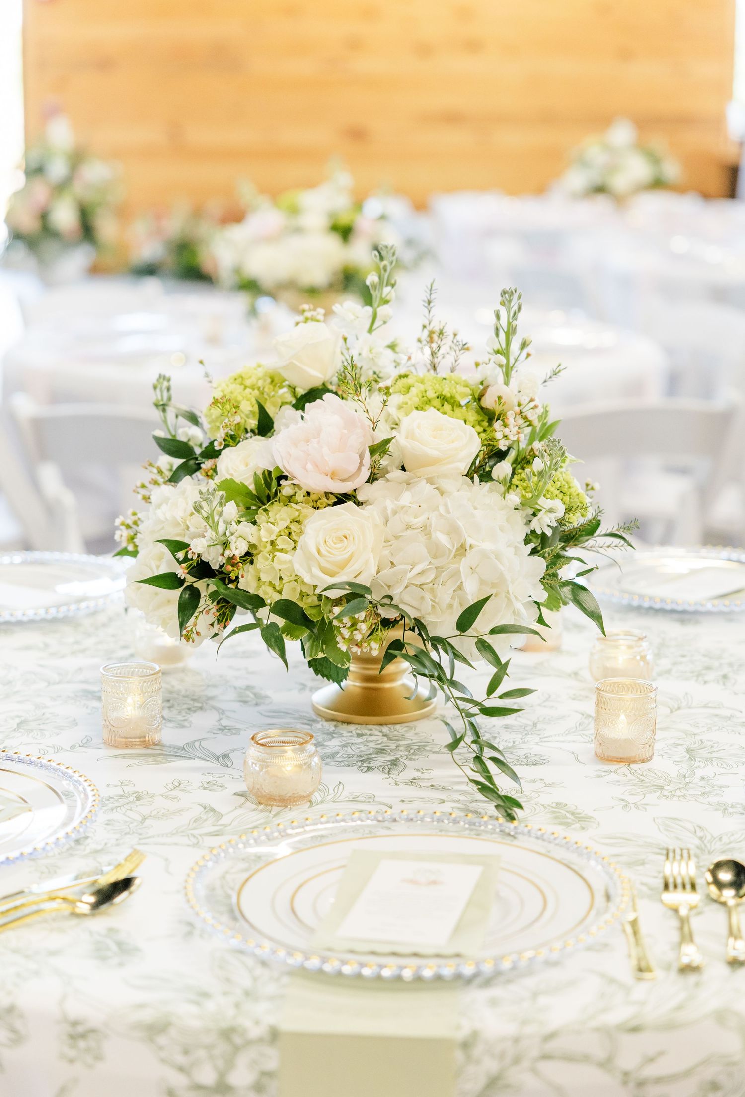 White and blush wedding centerpiece with roses and hydrangeas in a gold compote vase on patterned linen.