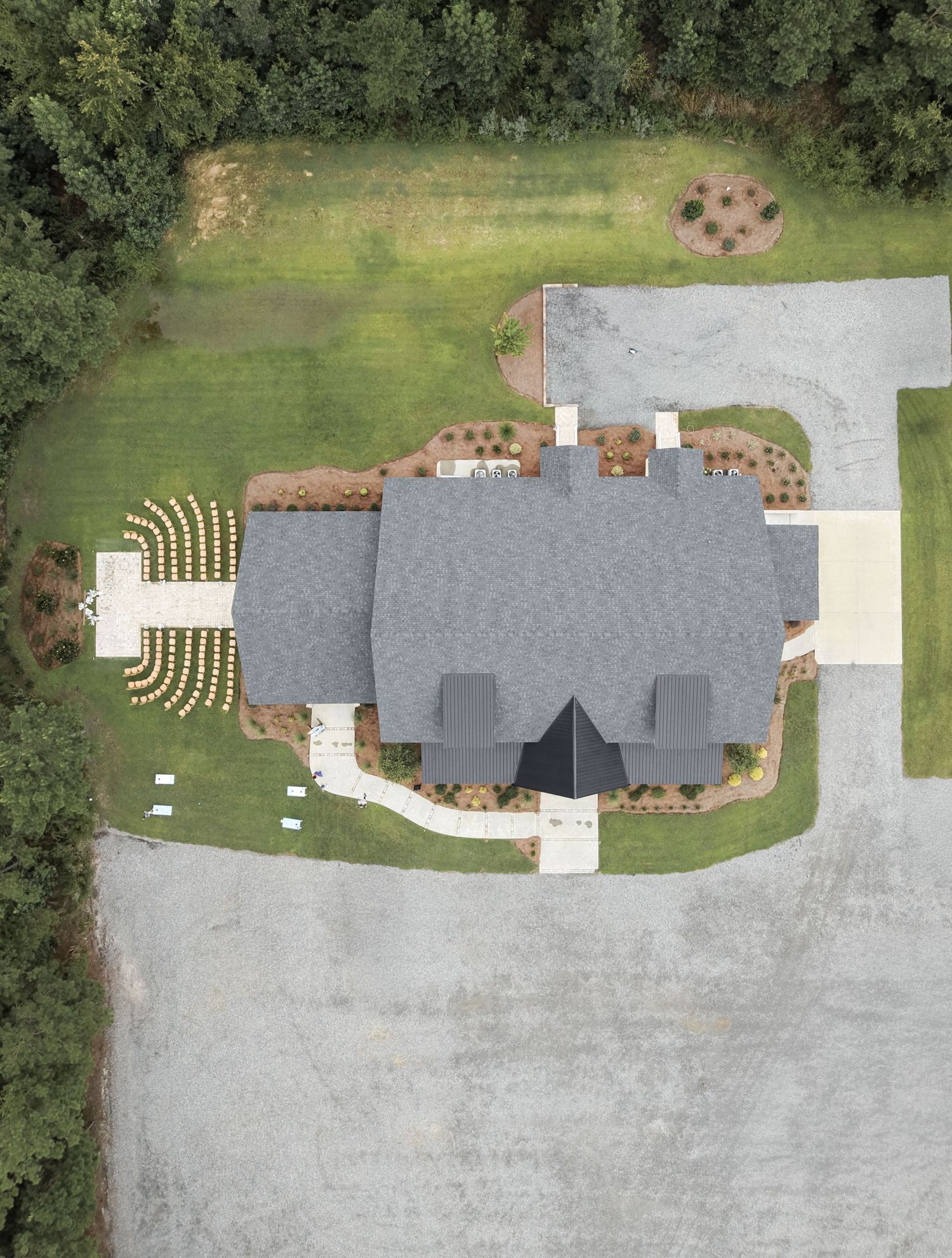 Aerial view of a large gray-roofed house with manicured lawn, circular driveway, and surrounding trees.