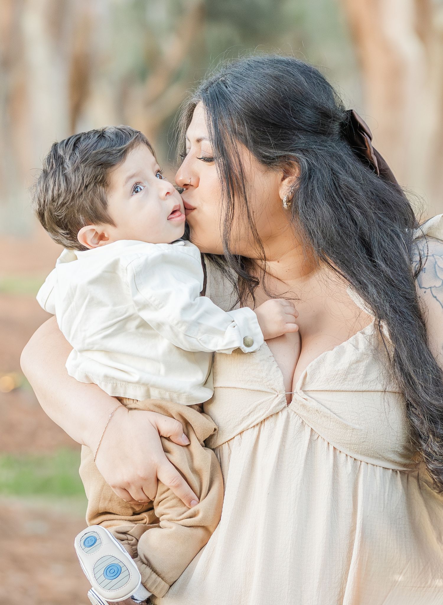 A tender moment captured between mother and child in cream-colored outfits against a natural outdoor backdrop.