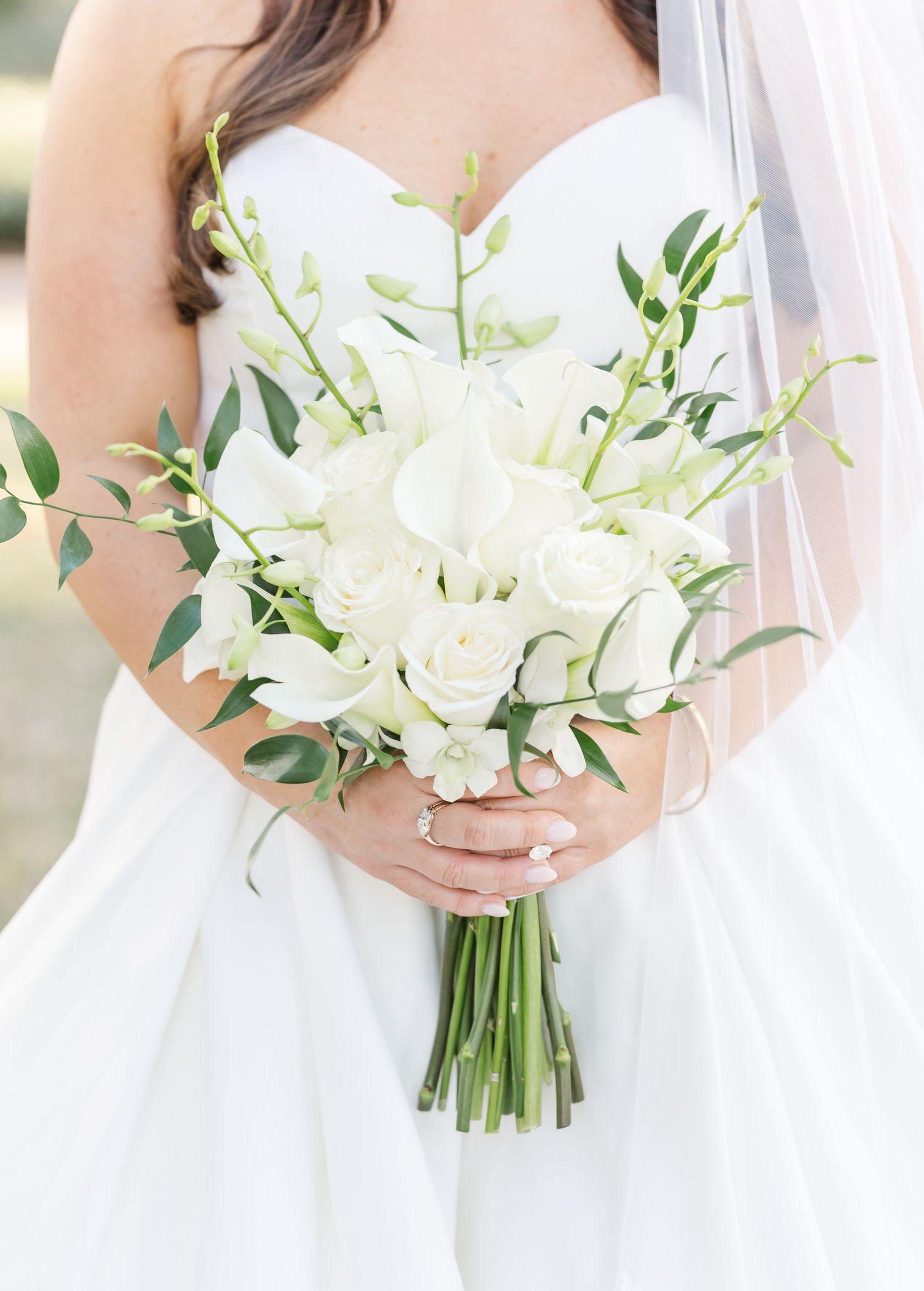 White bridal bouquets with delicate greenery and stems wrapped in ribbon are held against white dresses.