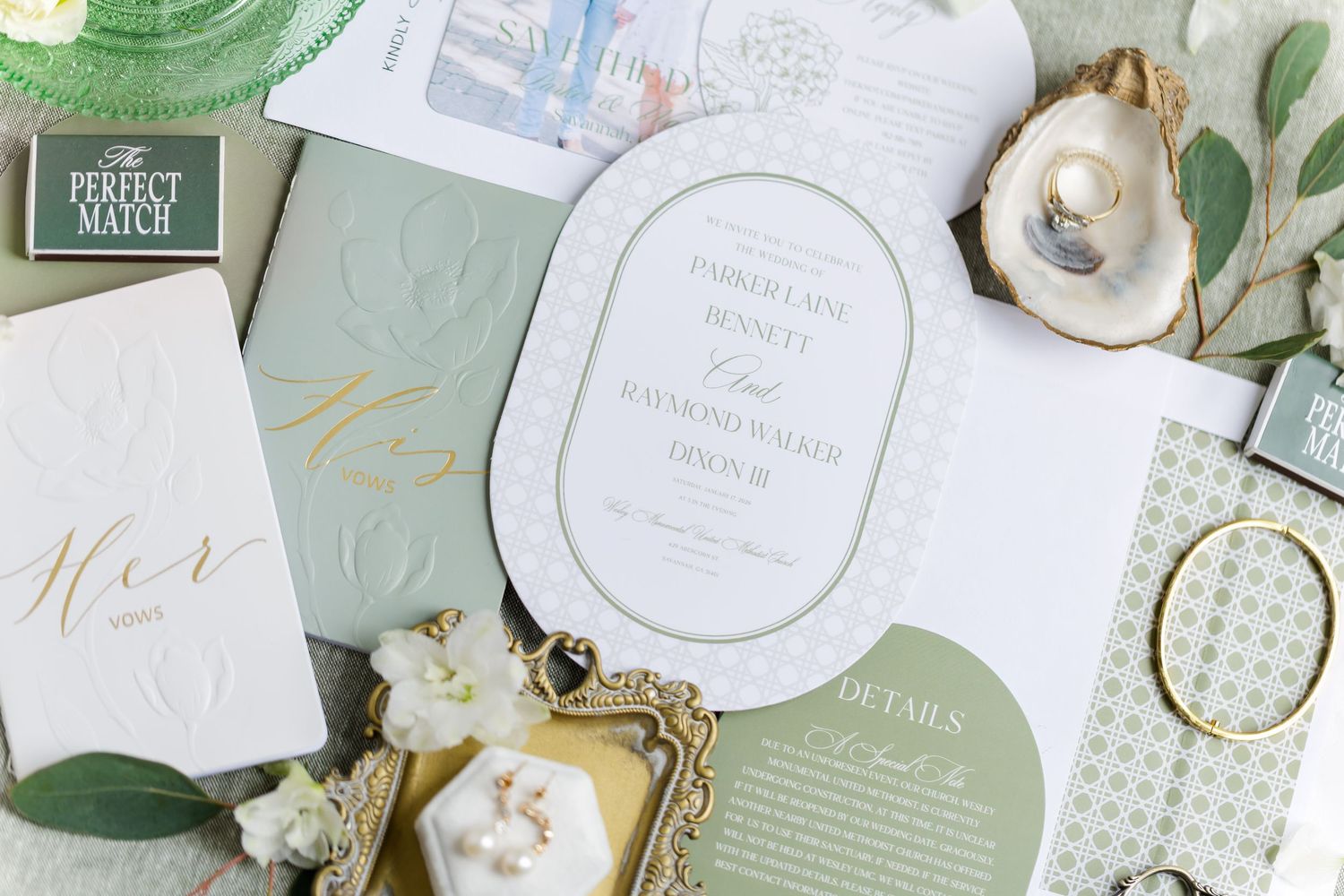 Flat lay of wedding stationery featuring sage green and white invitations with gold calligraphy and botanical elements.