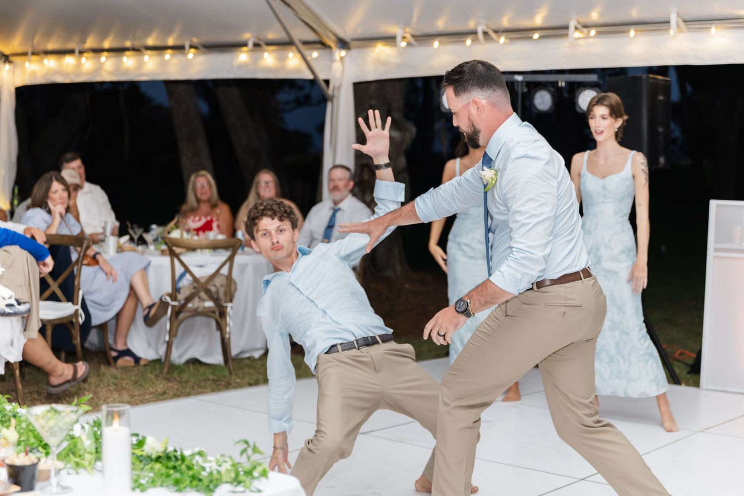 Wedding reception guests dancing and celebrating on a white dance floor under a tent at night.