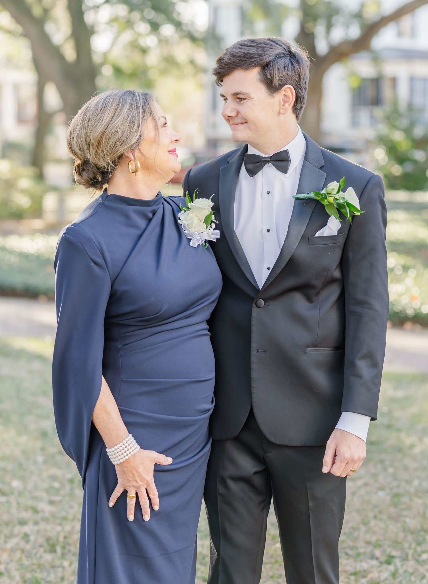 Formal wedding portraits of couple with family member in navy dress on garden grounds.