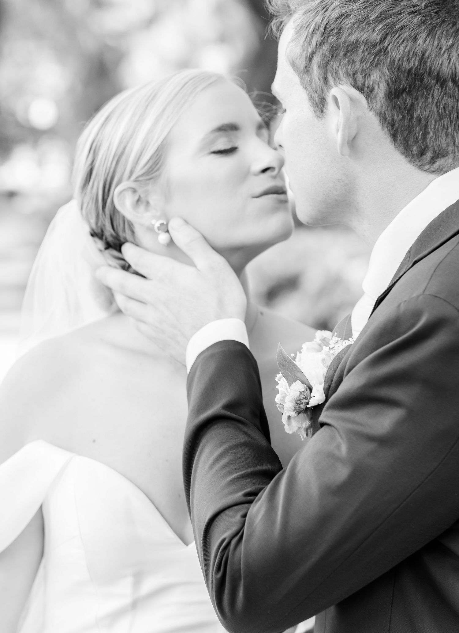 Black and white romantic wedding photo of a tender moment between bride and groom during their first kiss.