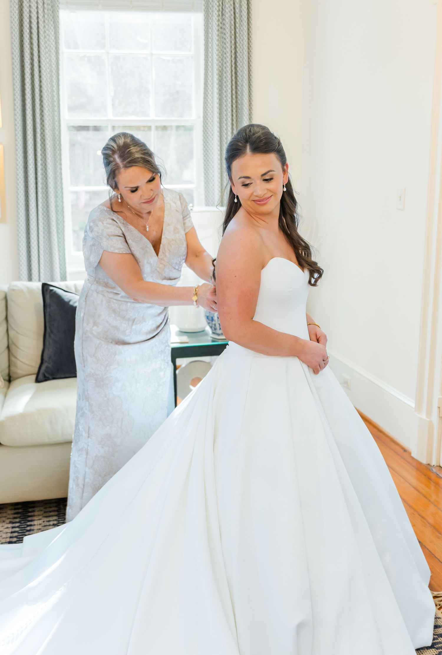 A bride in a white ballgown wedding dress gets help with final adjustments before the ceremony.