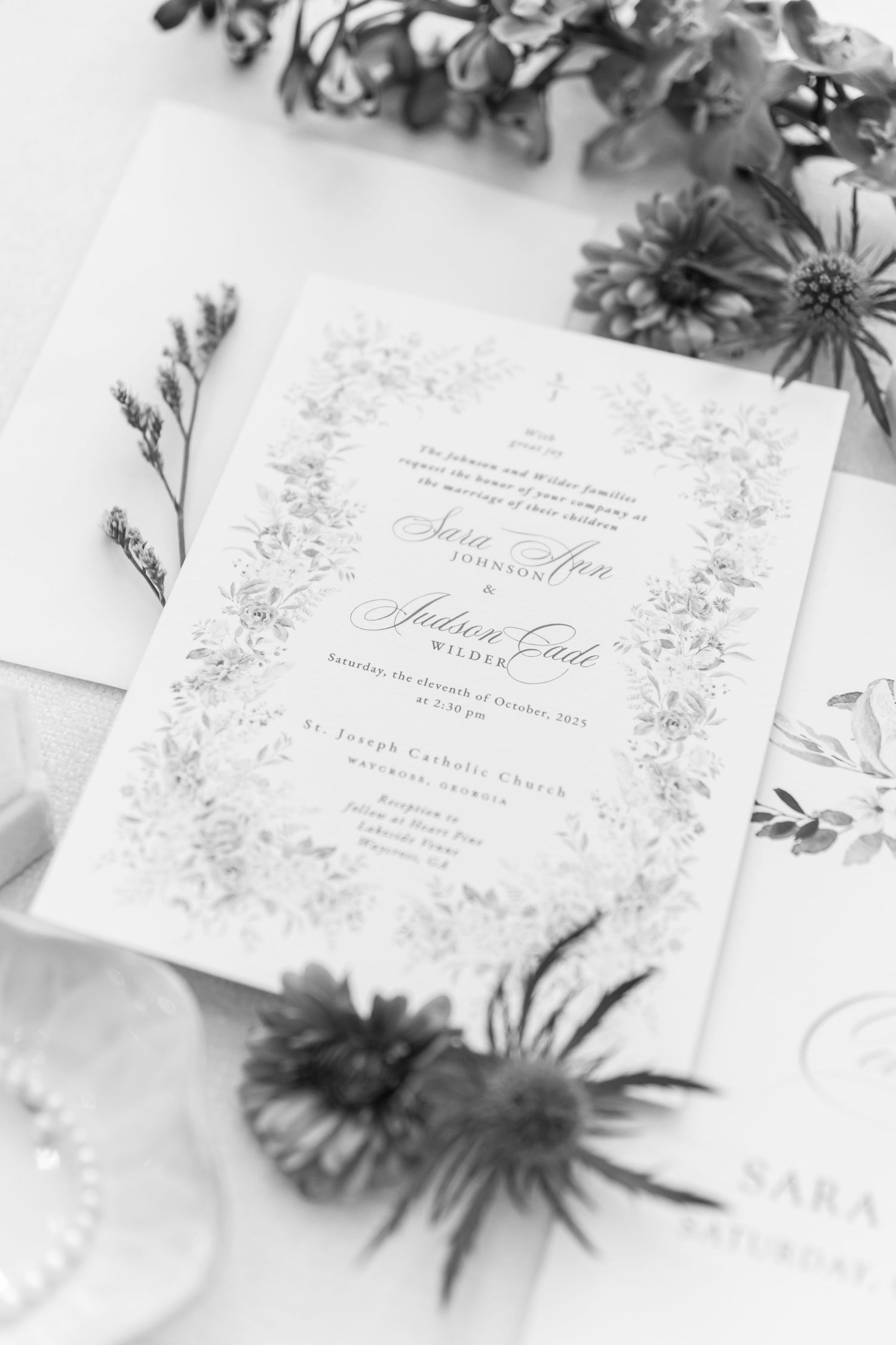 Elegant white wedding invitations with delicate floral designs and calligraphy text arranged on a light surface.