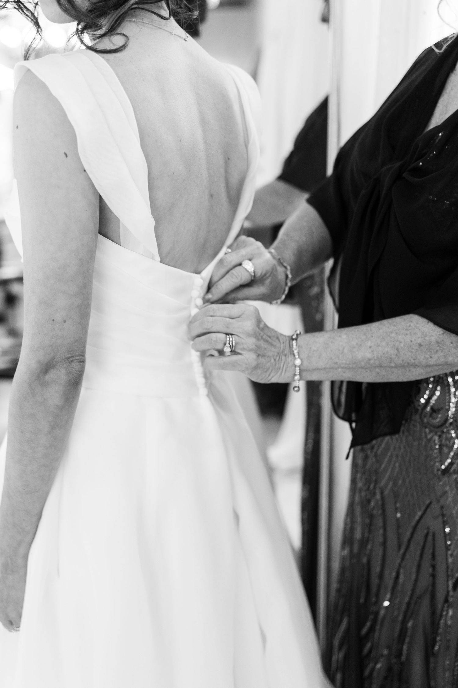 A bride in a white wedding dress stands with guests wearing black dresses at a formal event.