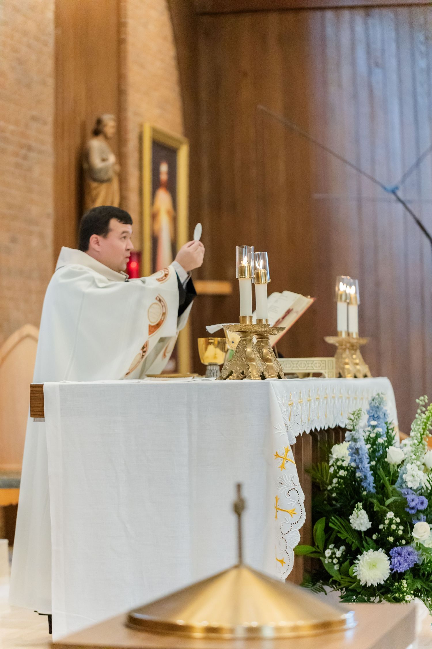 White-clothed altar decorated with floral arrangements and candles during a Catholic mass.