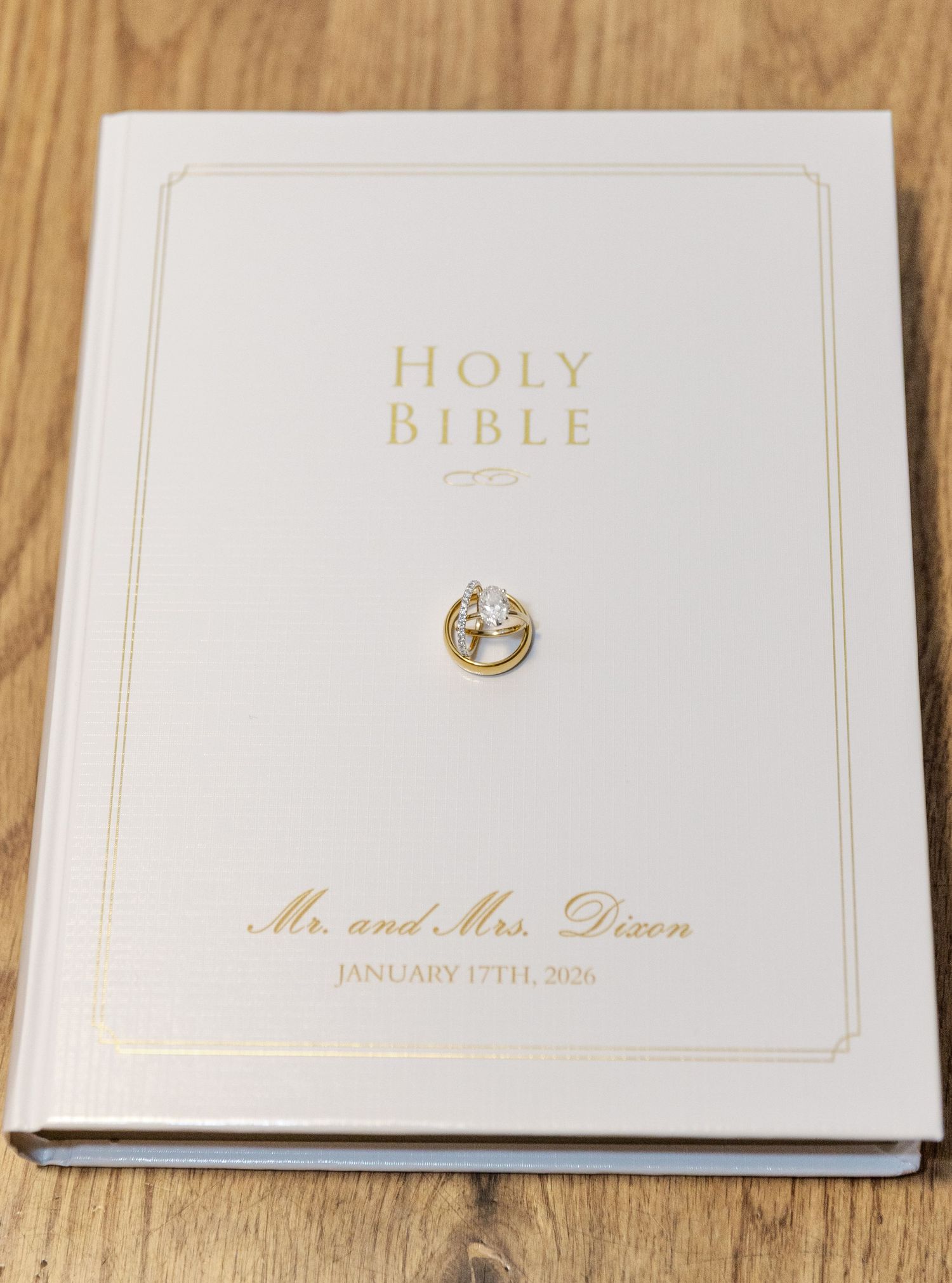 White wedding photo albums and Holy Bible with gold lettering arranged on wooden surface.