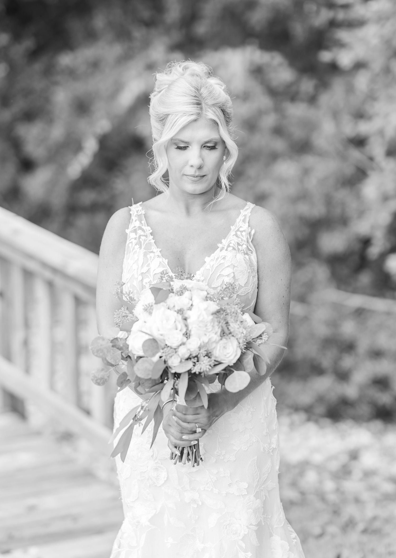 Black and white portrait of a bride in a lace wedding dress holding a romantic bouquet in an outdoor setting.
