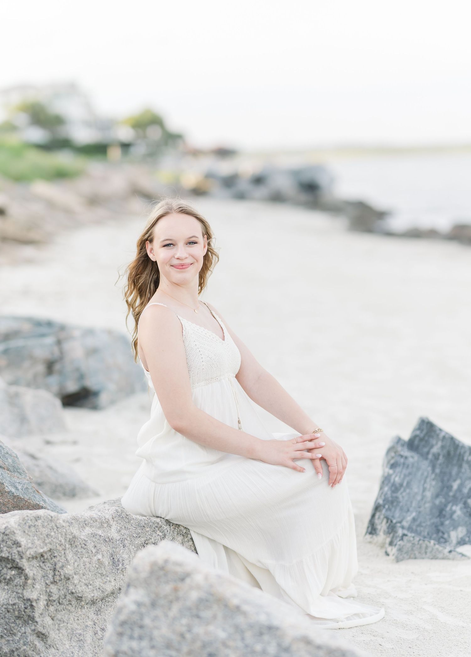 A dreamy coastal portrait on rocky beach with white dress and soft lighting.