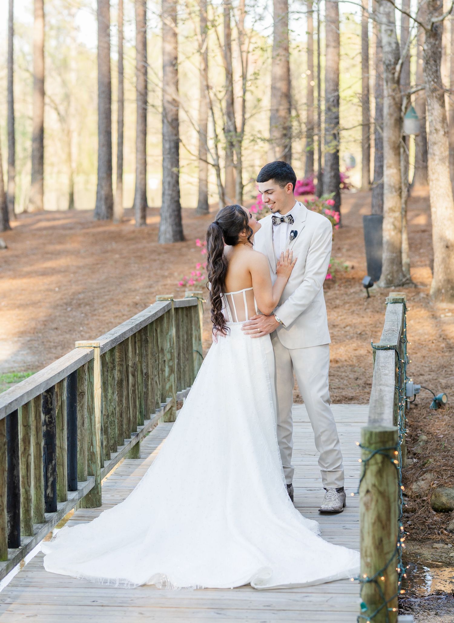 Bride and groom share a romantic moment on a wooden bridge surrounded by tall pine trees.