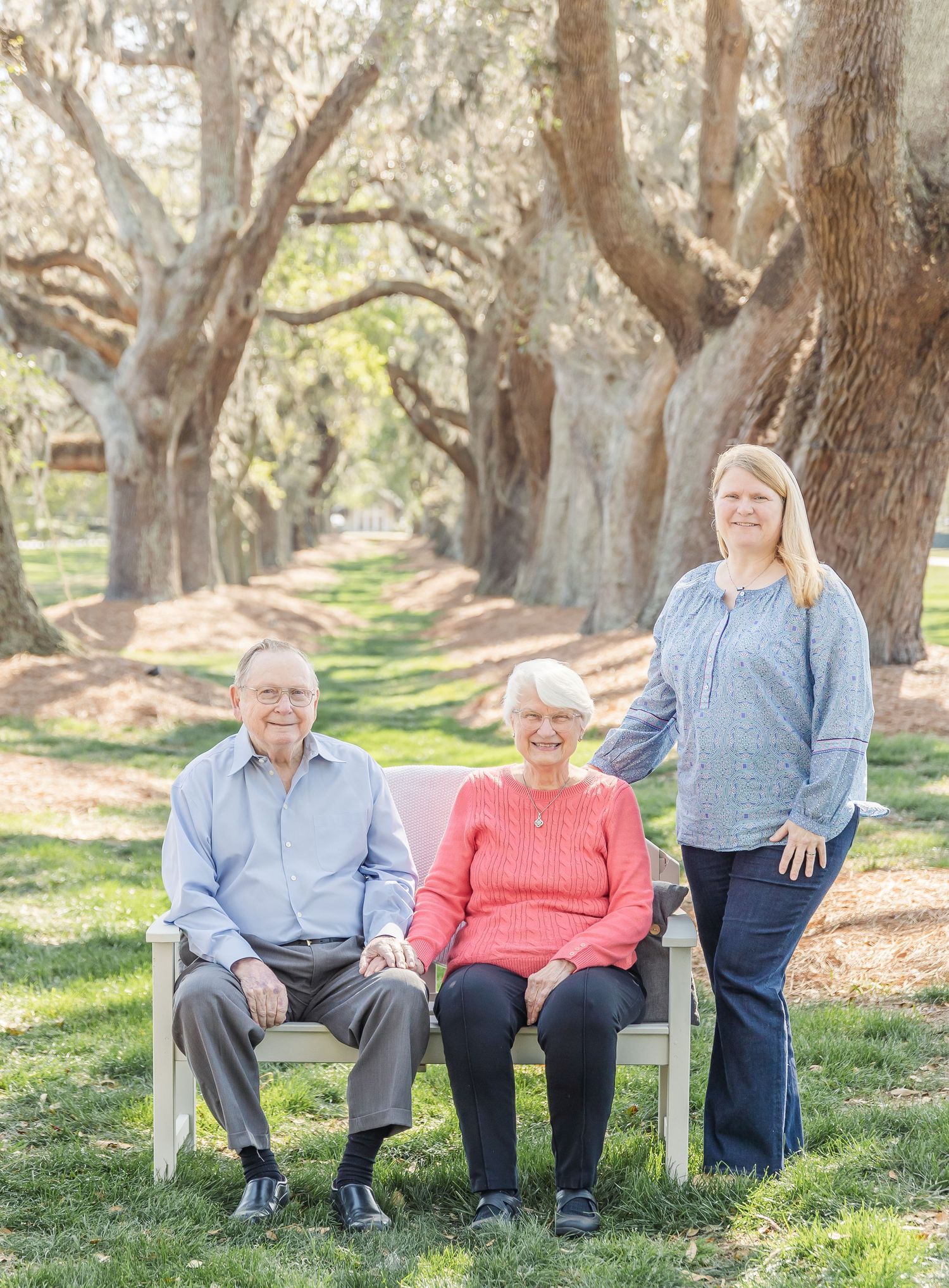 Family portrait with three generations on white bench beneath Spanish moss draped oaks.