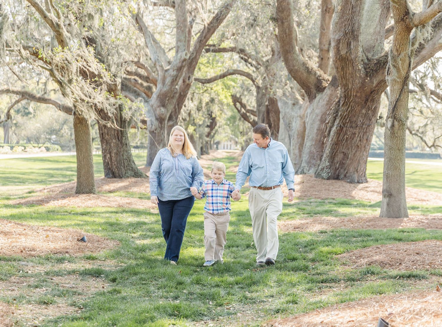 Family of three strolls together along scenic path surrounded by massive oak trees.