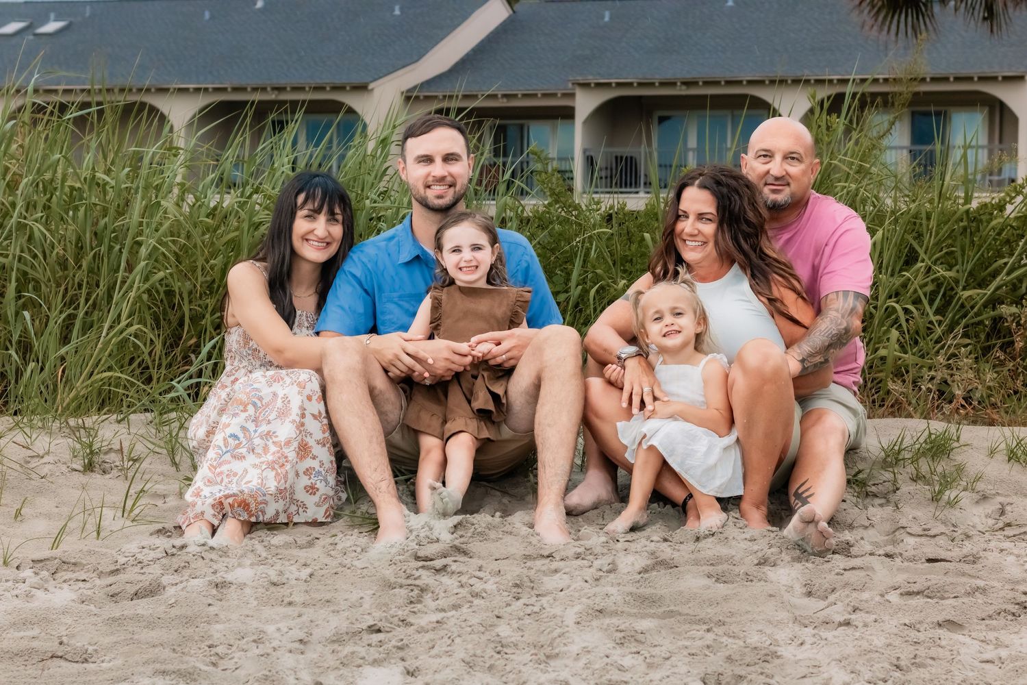 Family beach portrait with everyone sitting together on sandy shore.