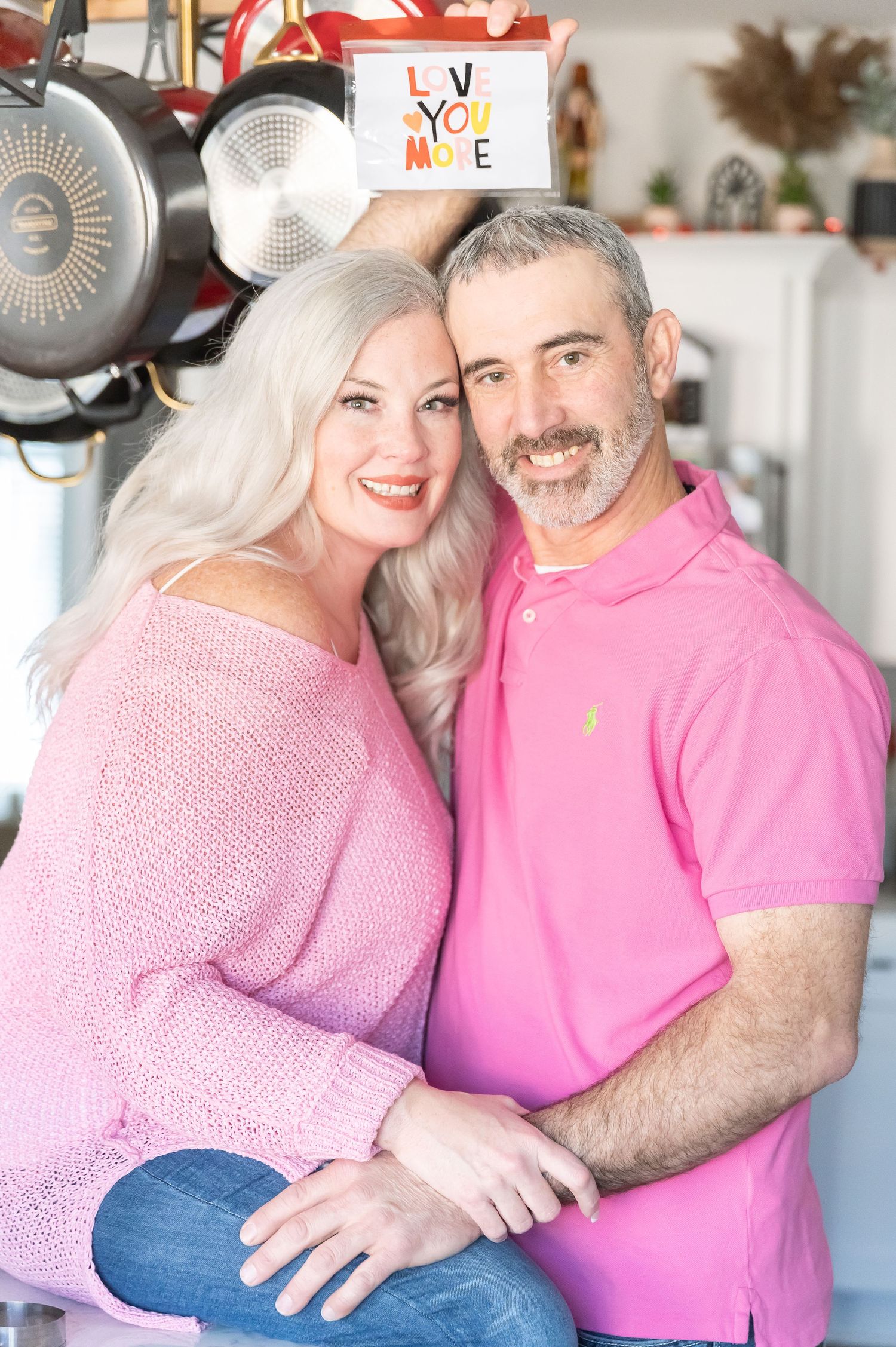A loving couple in coordinated pink outfits poses for a photo in their decorated kitchen.