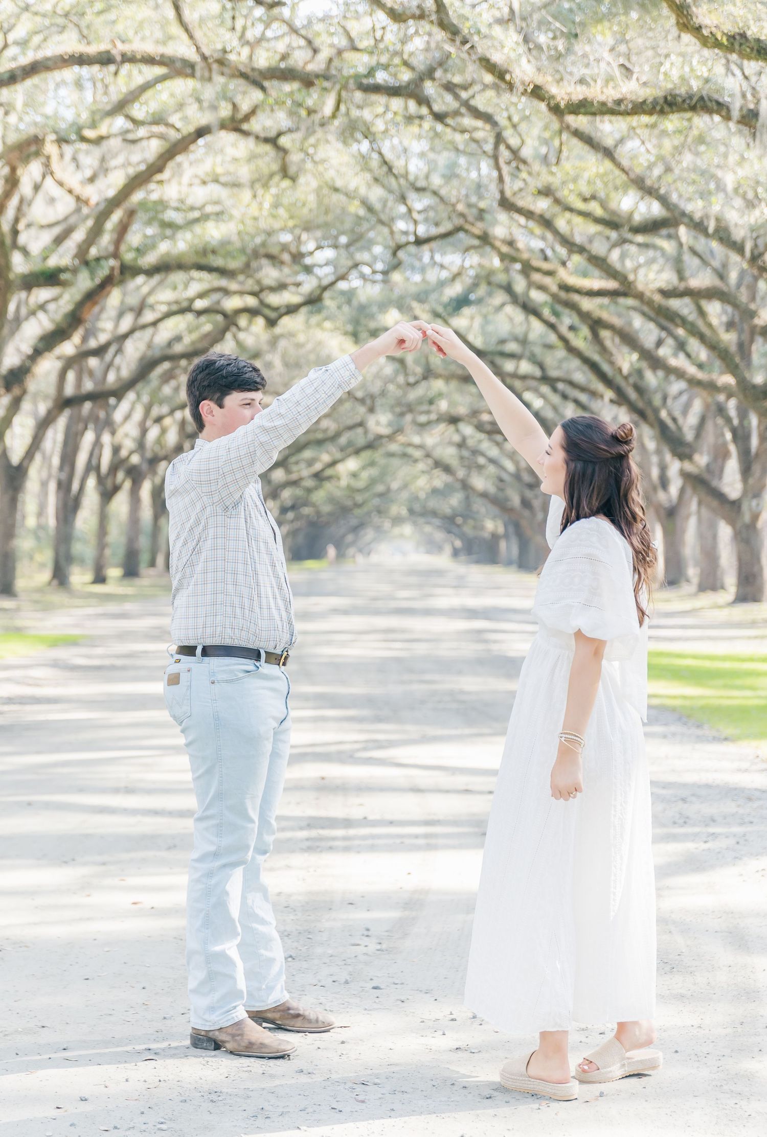 A couple hold hands high while dancing on a tree-lined pathway.