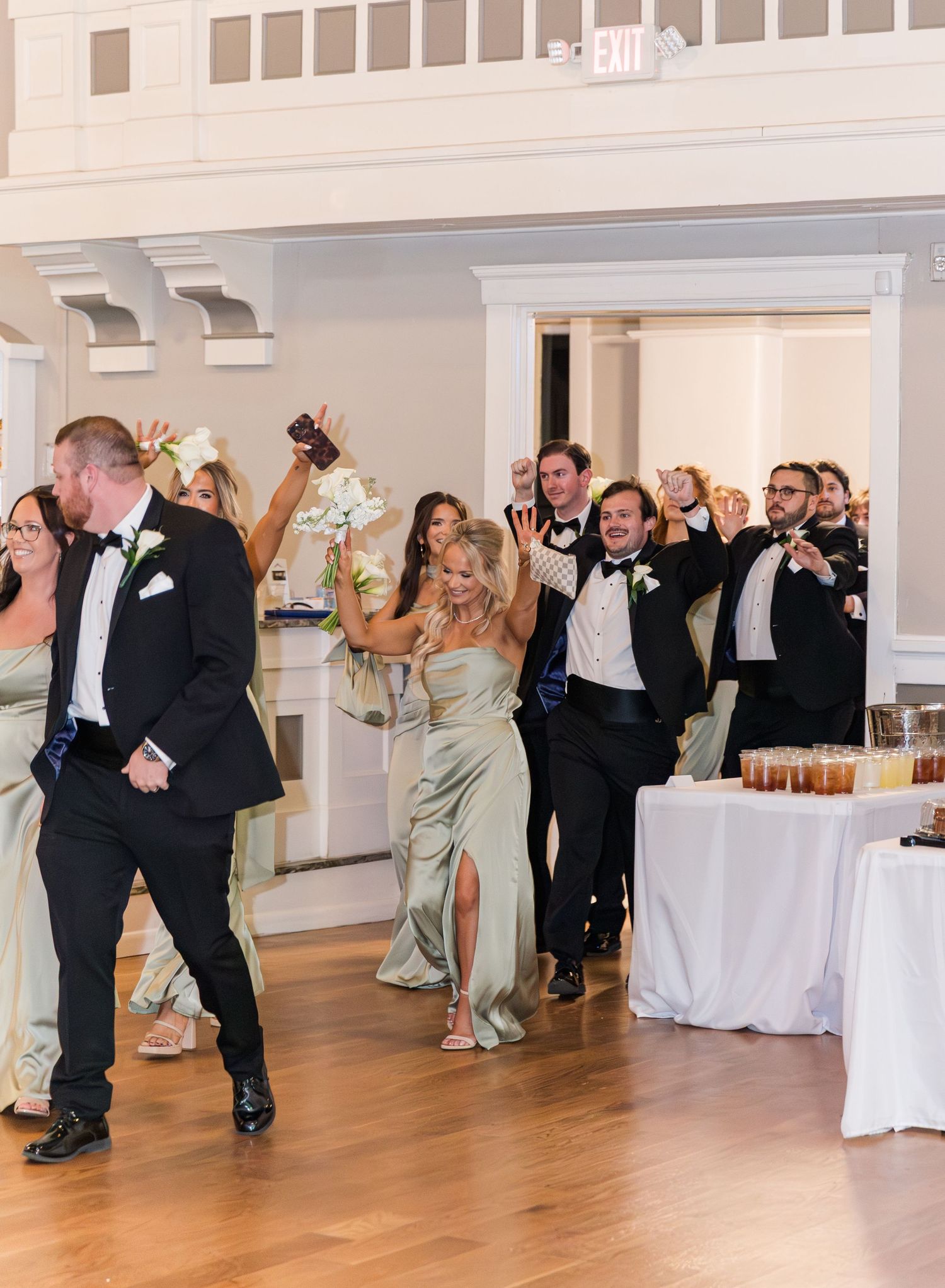 Wedding party makes a grand entrance into the reception hall, cheering and celebrating with raised arms.
