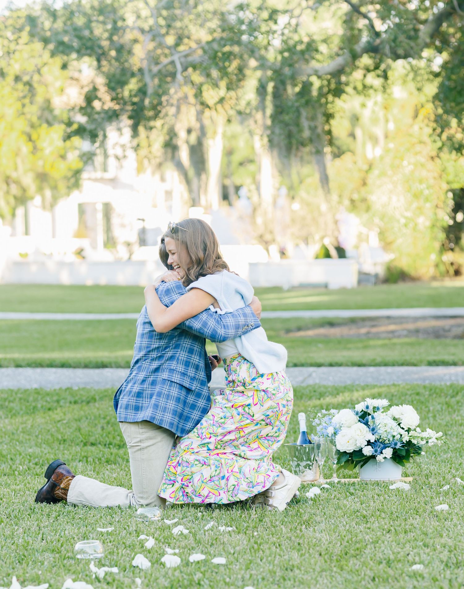 Two people embrace on a grassy lawn with white flowers and decorations.