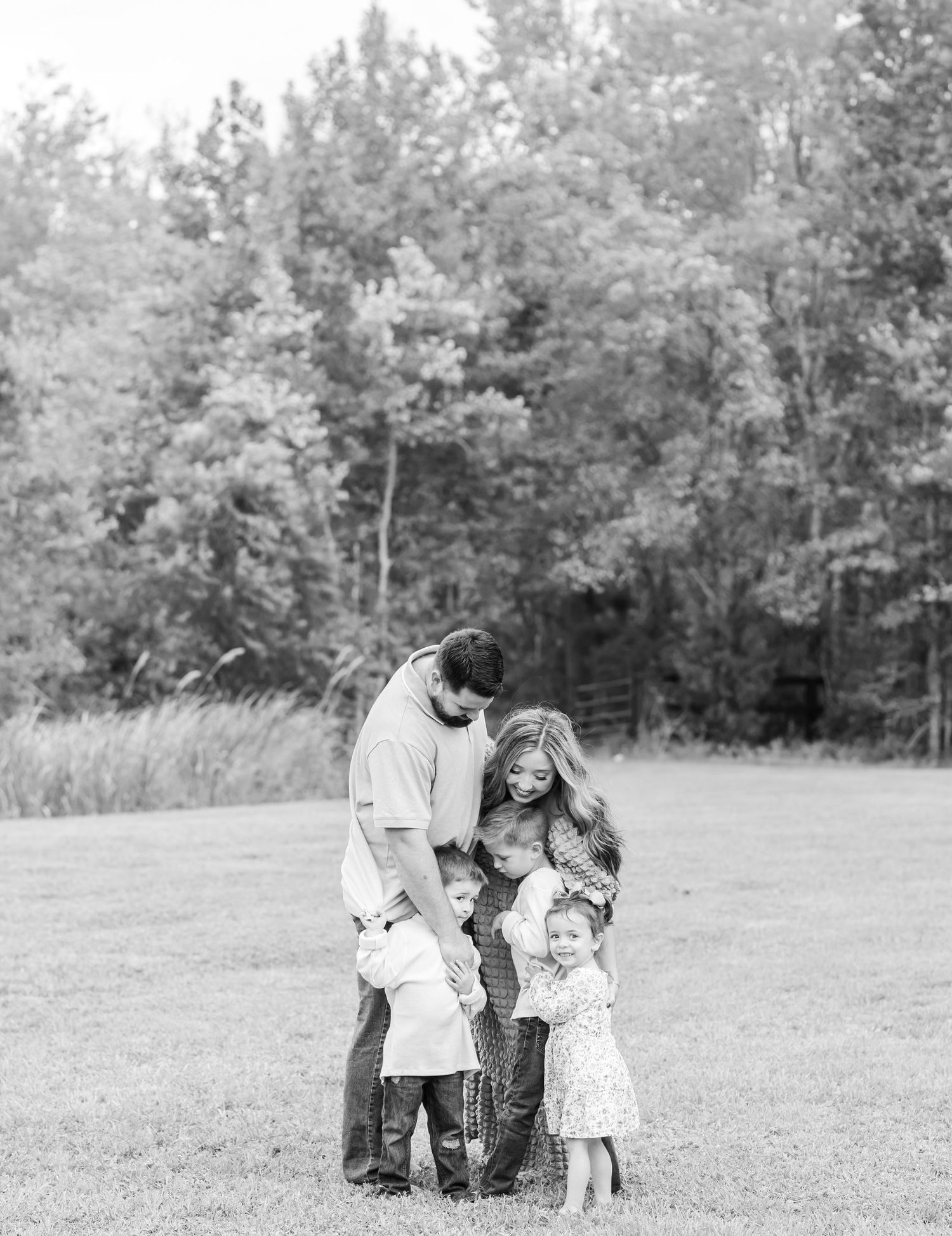 A black and white photo series shows a couple embracing and walking together in a grassy field with trees in the background.