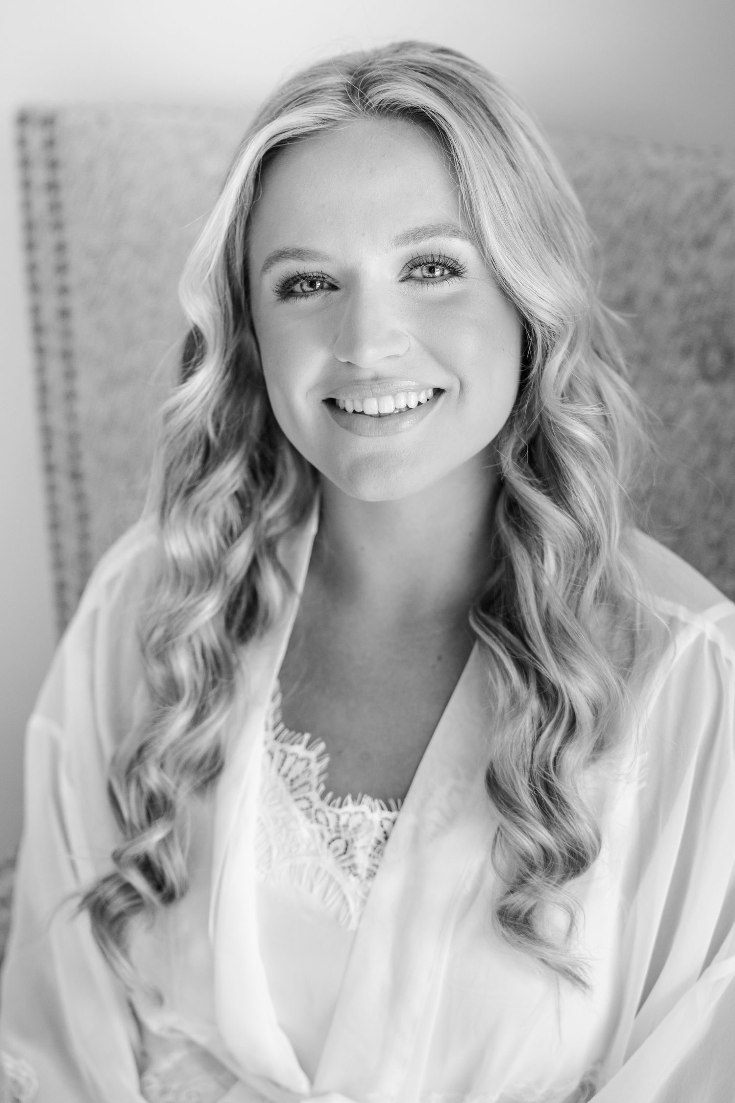 Black and white portrait of a smiling blonde bride in a silk robe with lace detail on her wedding day.