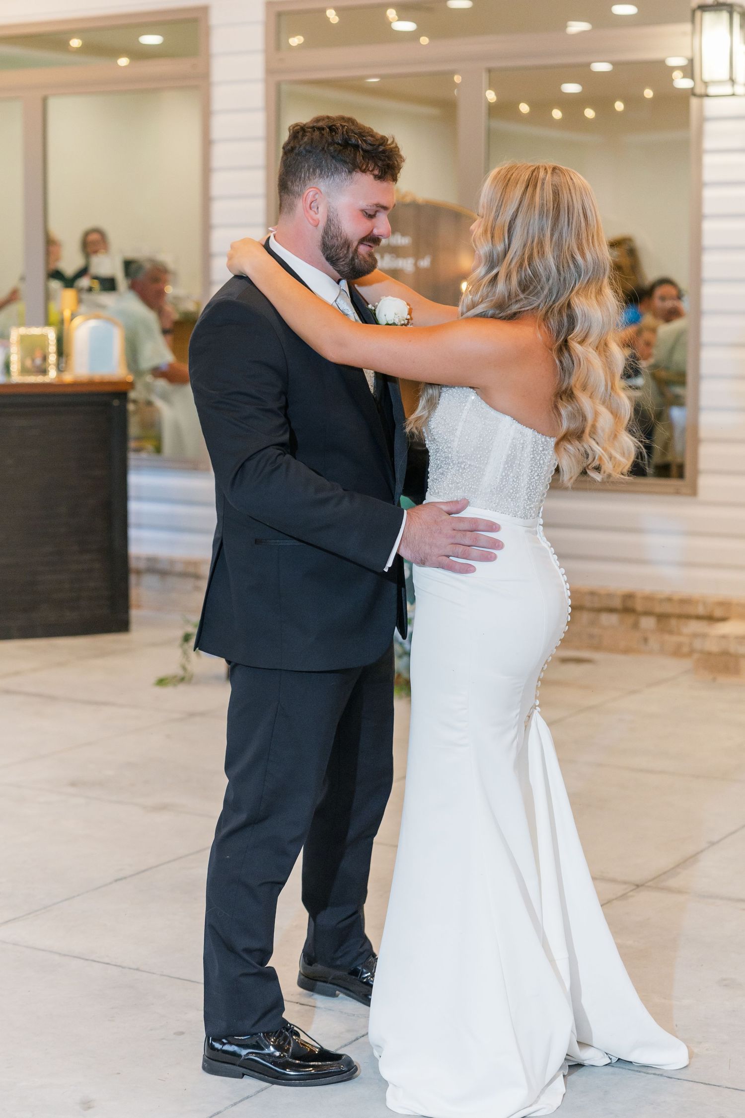 Bride and groom sharing their first dance outdoors at wedding reception under warm string lights.