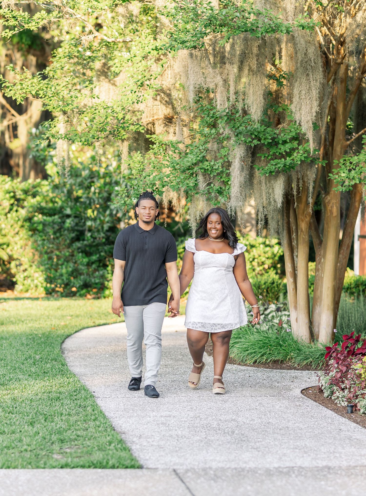 Couple strolling down a garden path with Spanish moss hanging from trees.