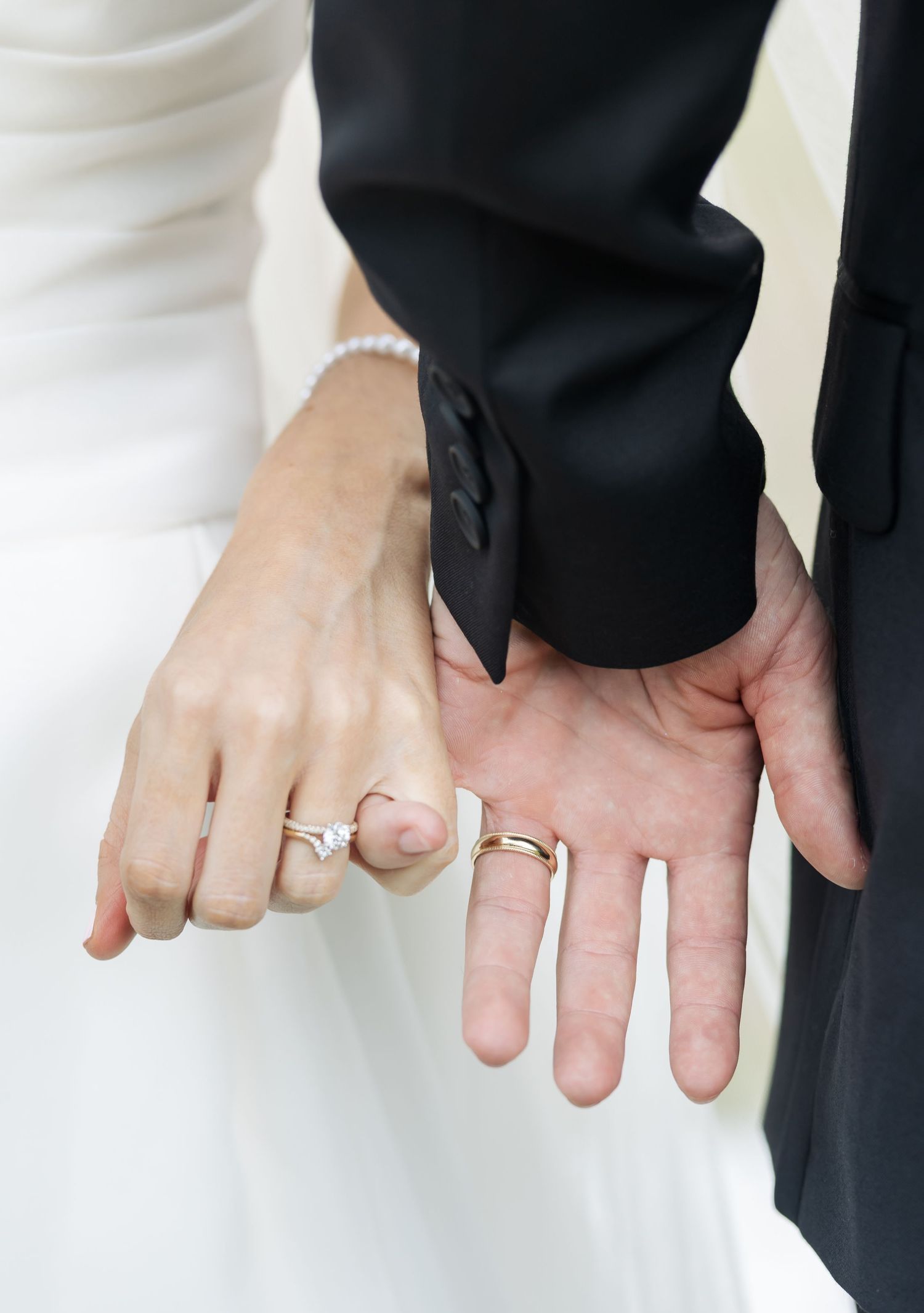 Close-up of newlywed couple's hands showing wedding rings against white dress and black suit.
