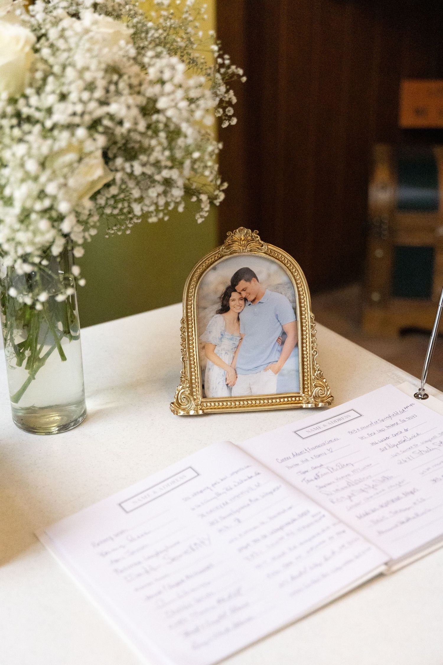 Framed photograph displayed next to white baby's breath flowers and handwritten notes on a guest book table.
