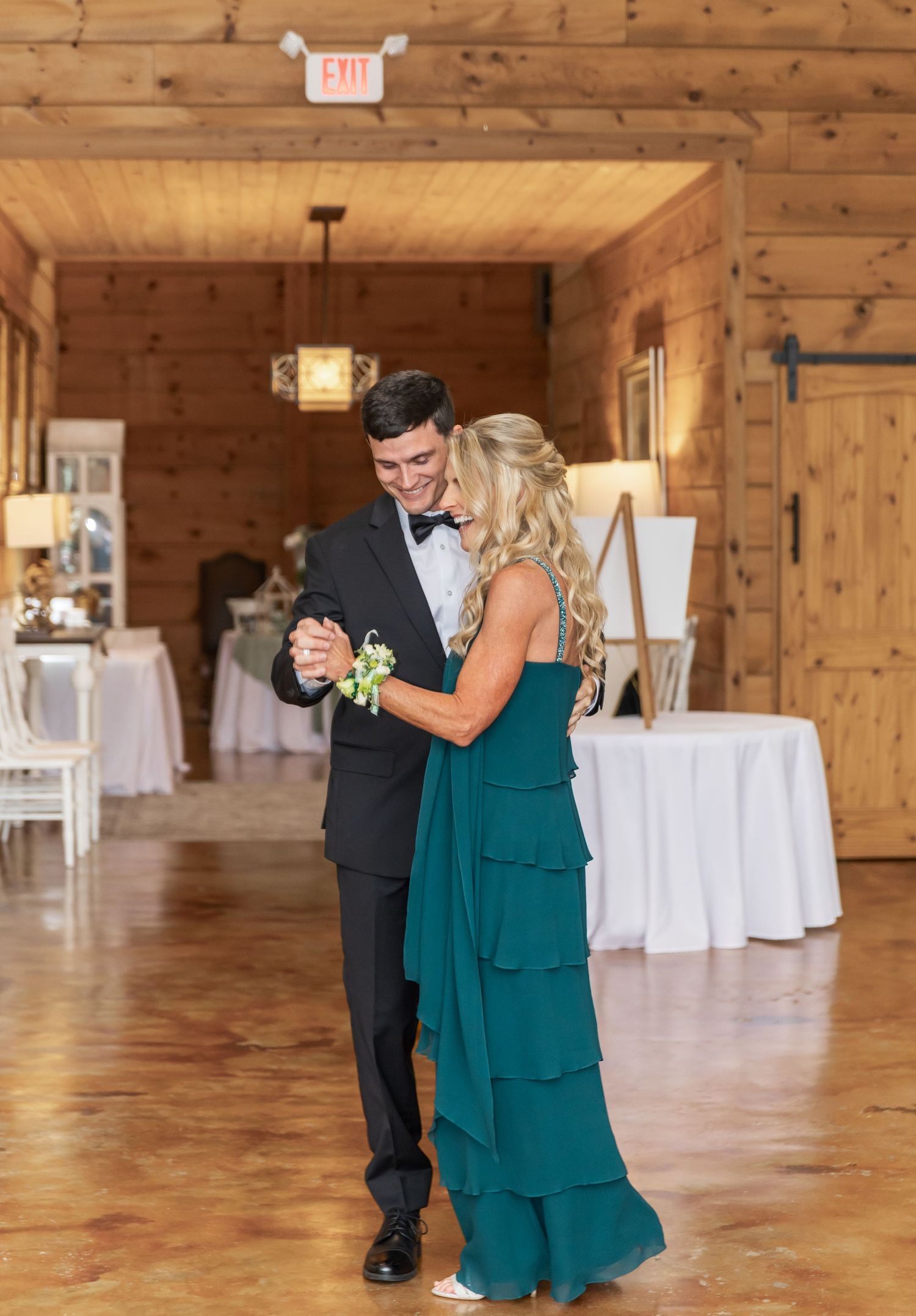 Couples dance together during a wedding reception in a warm wooden barn interior.