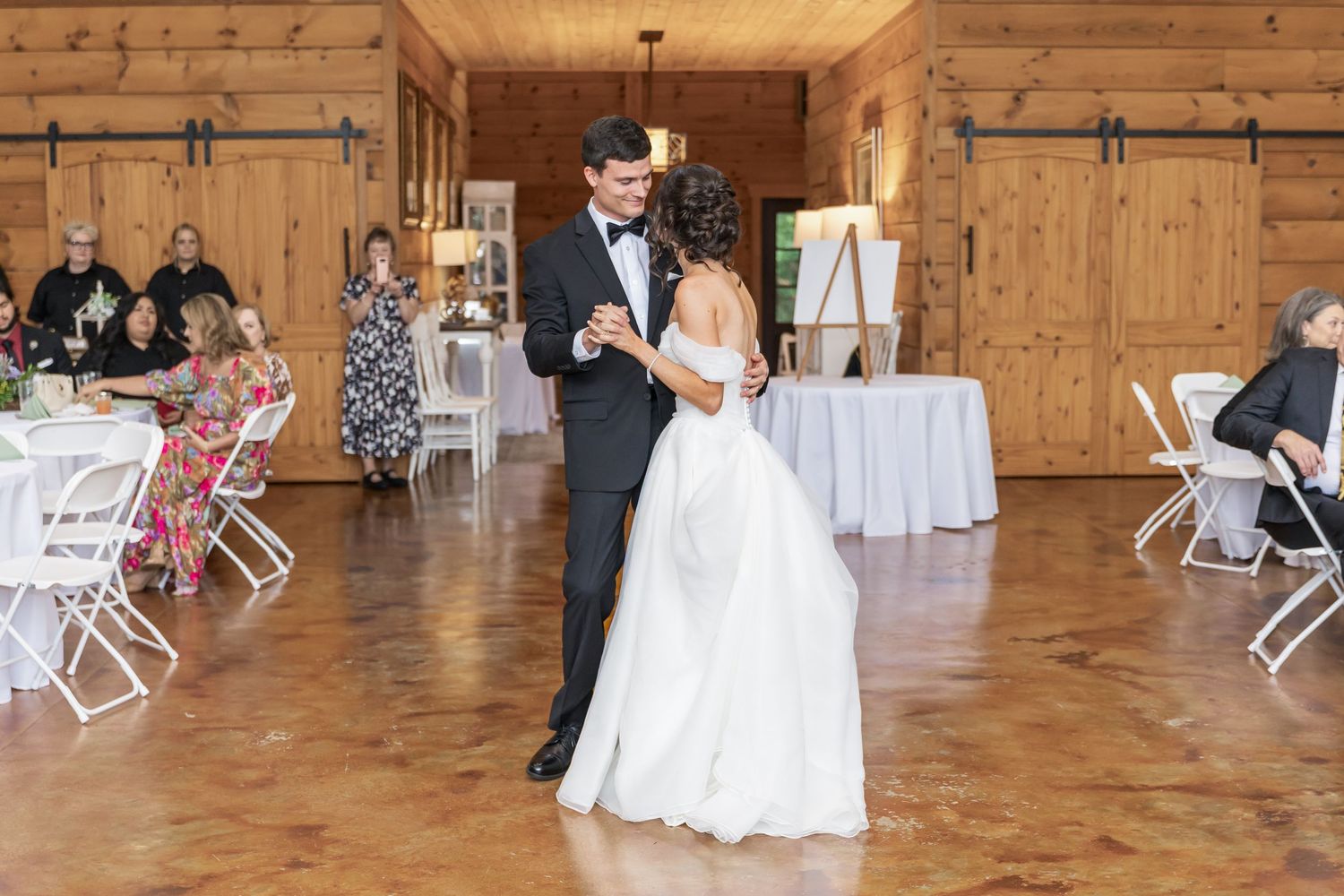 A rustic wooden barn venue decorated for a wedding reception with white chairs and elegant lighting.