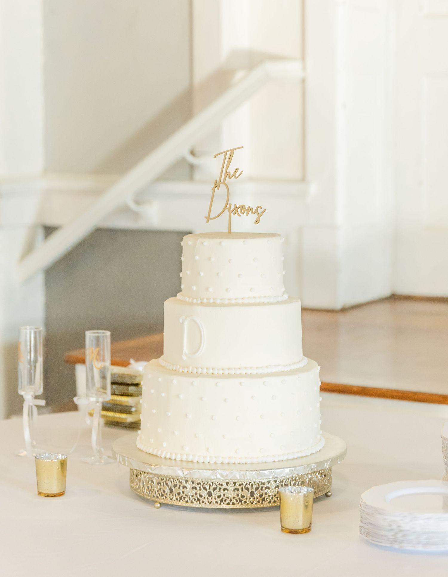 Simple white tiered wedding cake with gold topper on display in bright venue.