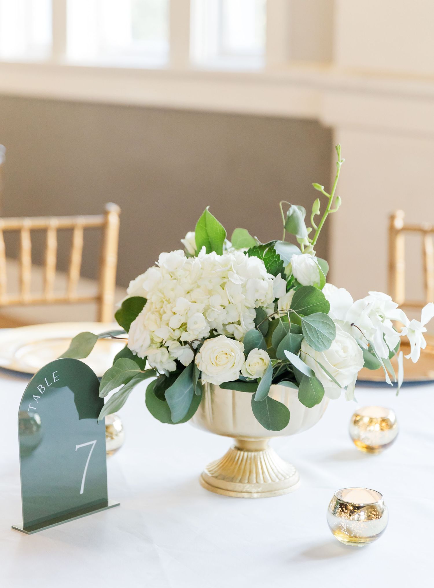 White hydrangea and eucalyptus centerpiece in gold vase with table number.